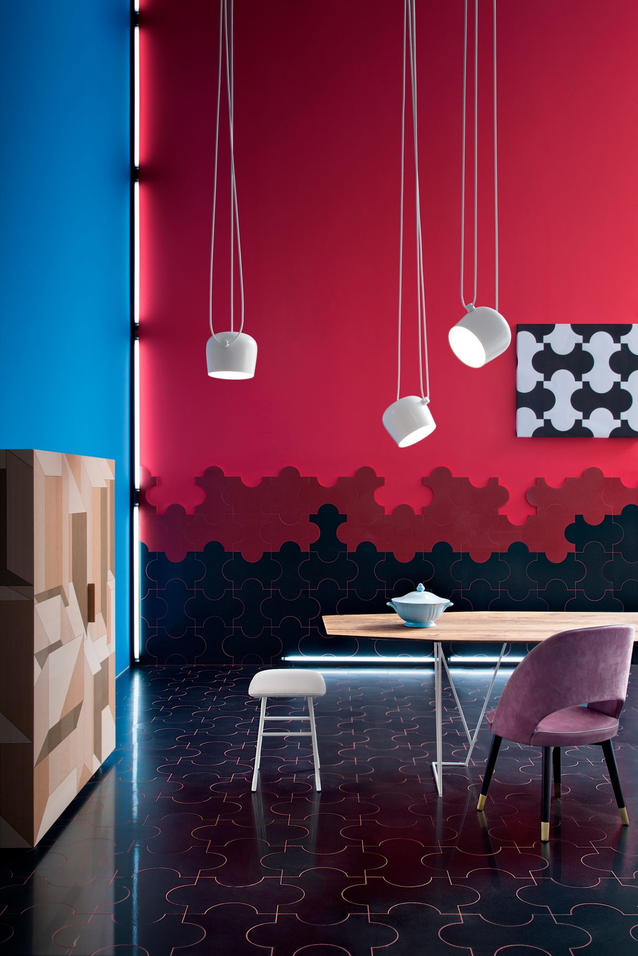 Drei weiße Aim Small Pendelleuchten von Flos hängen über einem Esstisch in einem farbenfrohen Raum.