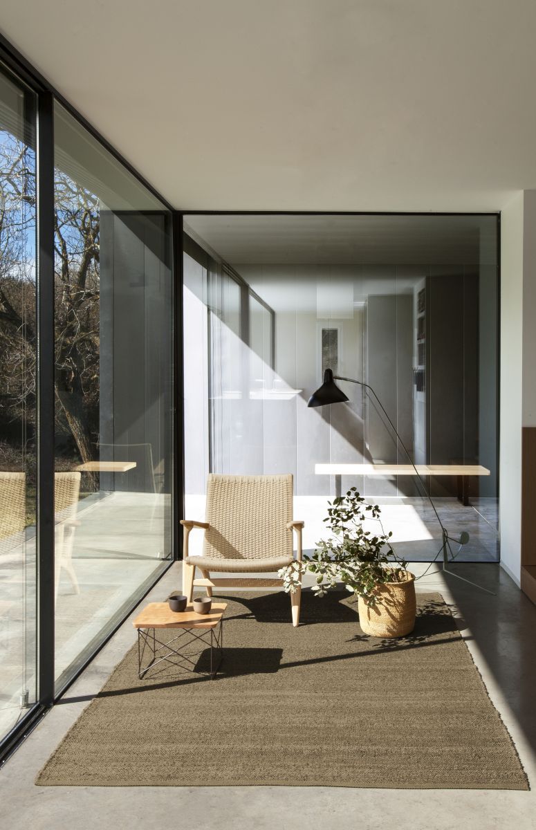 Brauner Nanimarquina Teppich "Herb" (250x350cm) im modernen Wohnzimmer mit Sessel und Pflanze.