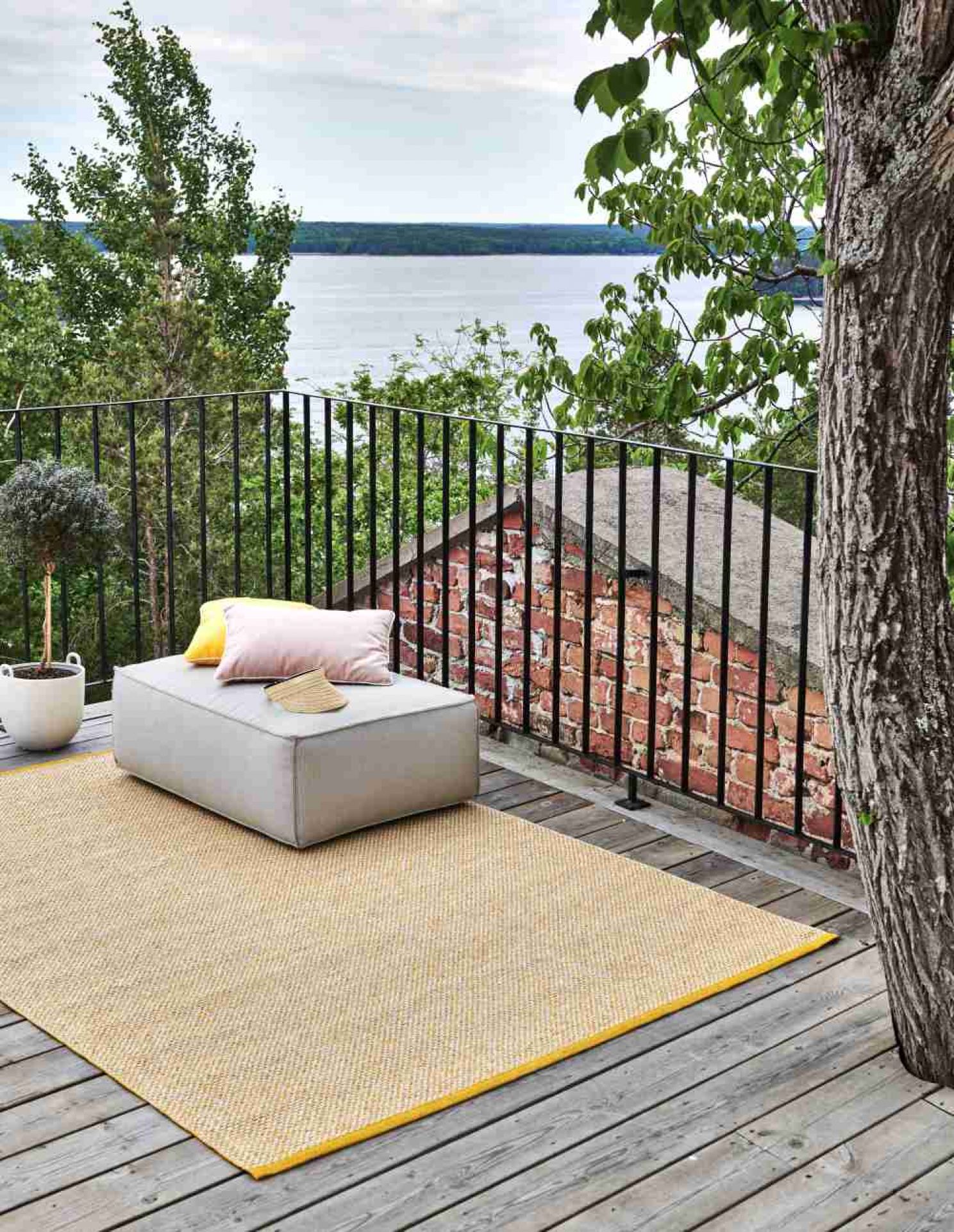 Effi Kunststoffteppich in Senfgelb (230x320 cm) von Pappelina auf Holzterrasse mit Sitzgelegenheit und Ausblick.