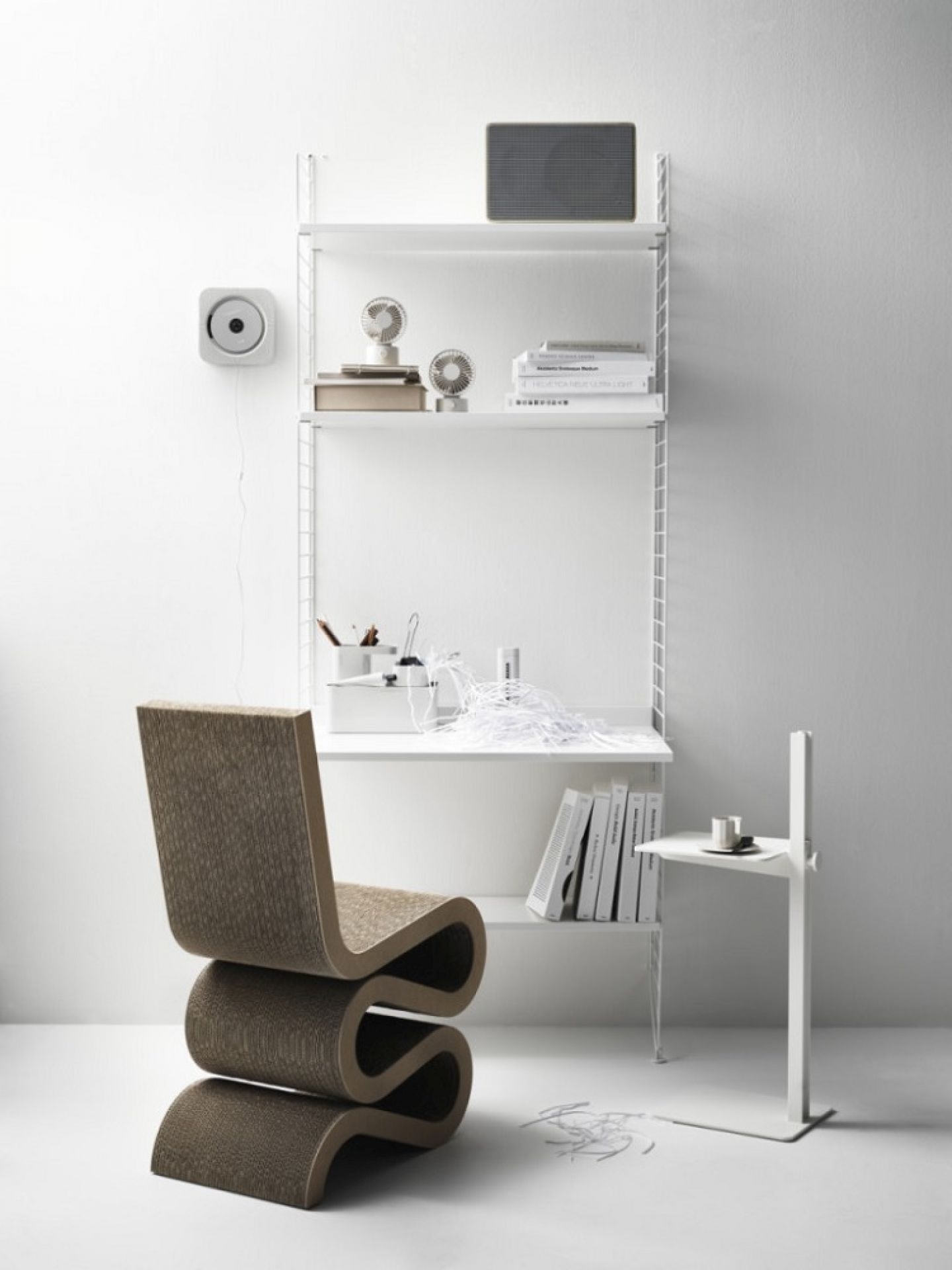 Minimalistisches Interieur mit String Furniture Regal und höhenverstellbarem Beistelltisch. Moderner Sidetable neben einem Design-Stuhl.