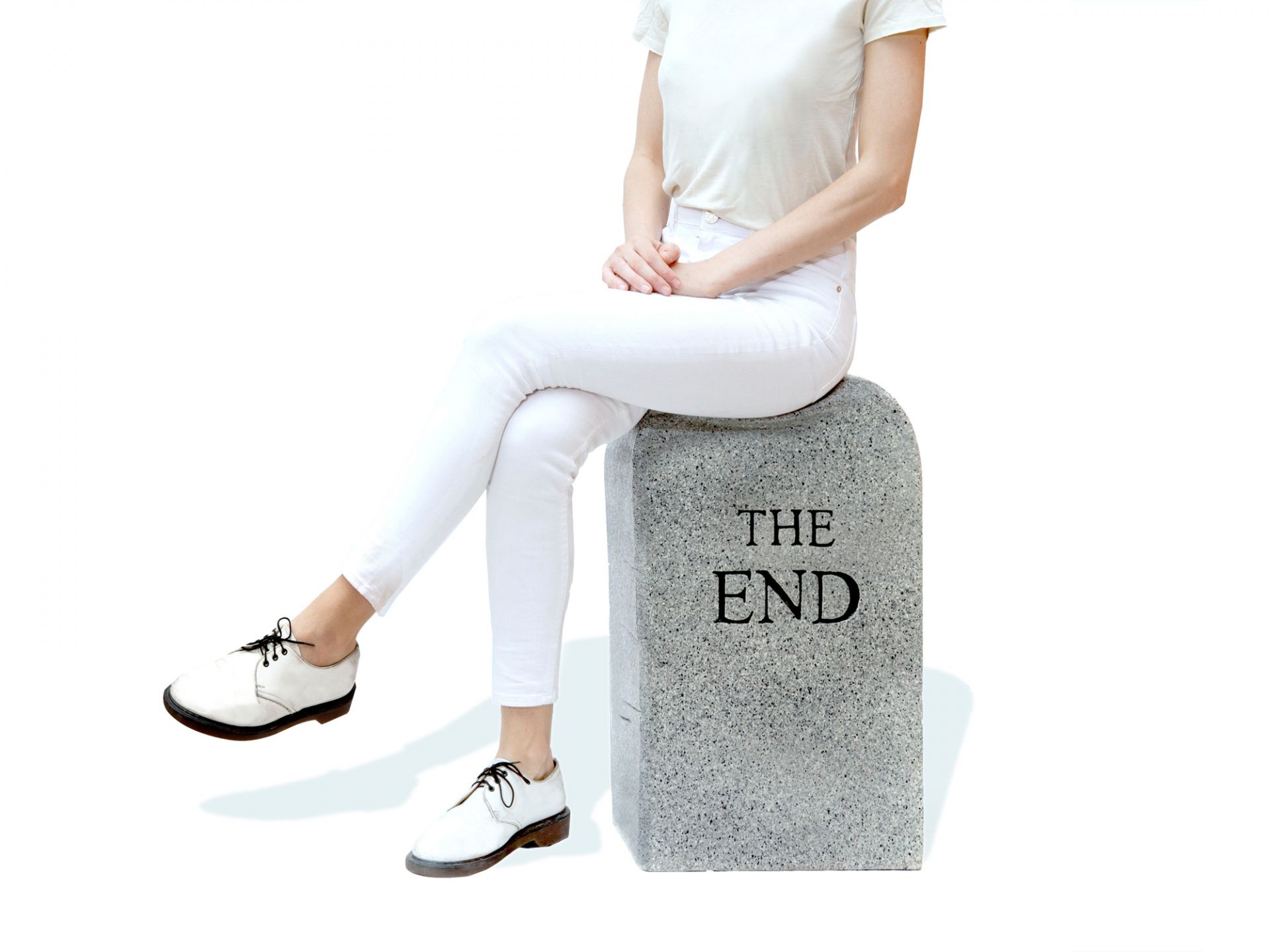 Frau sitzt auf grauem "The End" Hocker von Gufram, originelles Möbelstück für Wohnzimmer und Büro.