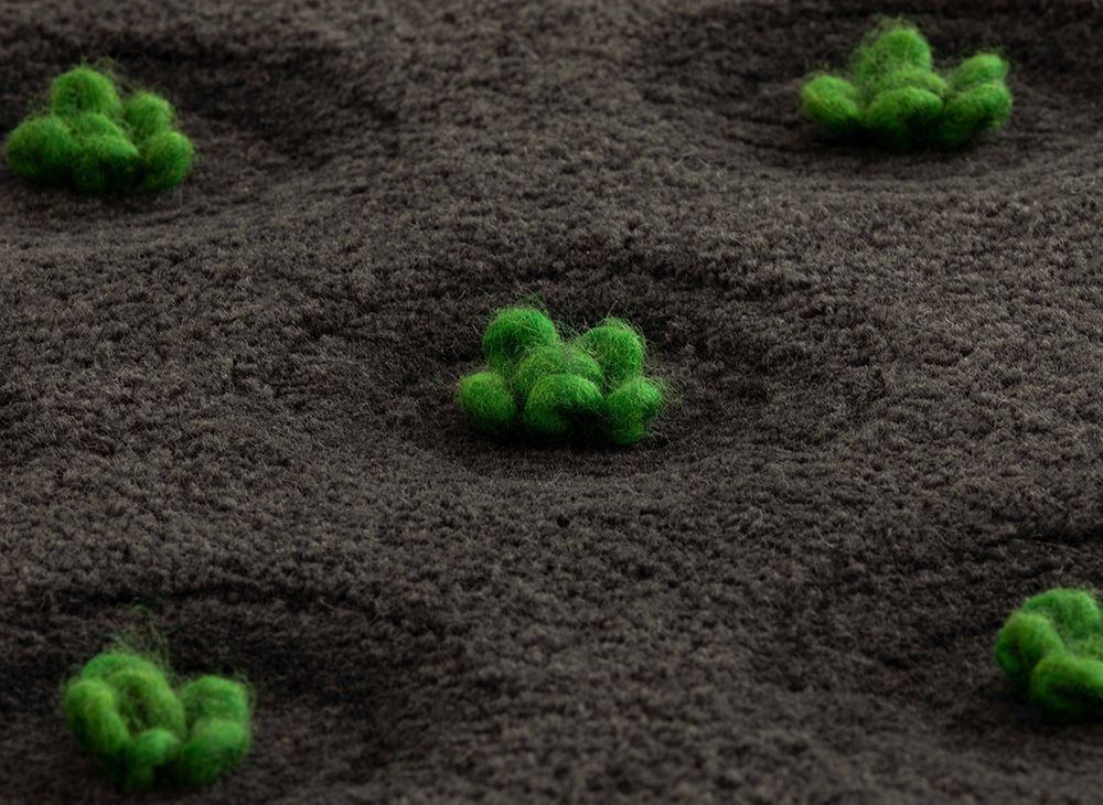 Detailaufnahme des La Geria Teppichs von Gan, runder Wollteppich mit grünen Akzenten.