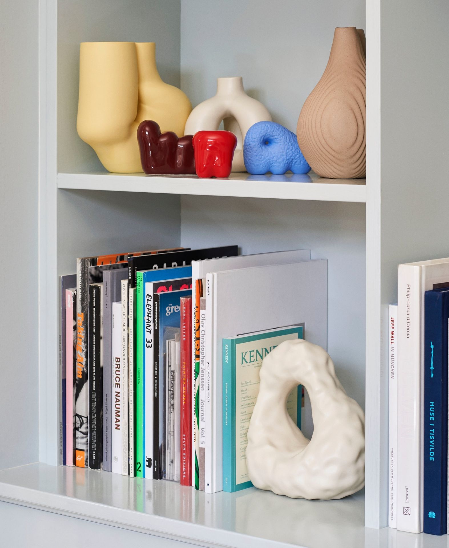 Regal mit Büchern und dekorativen Objekten, darunter eine weiße W&S Boulder Bookend Buchstütze von Hay.