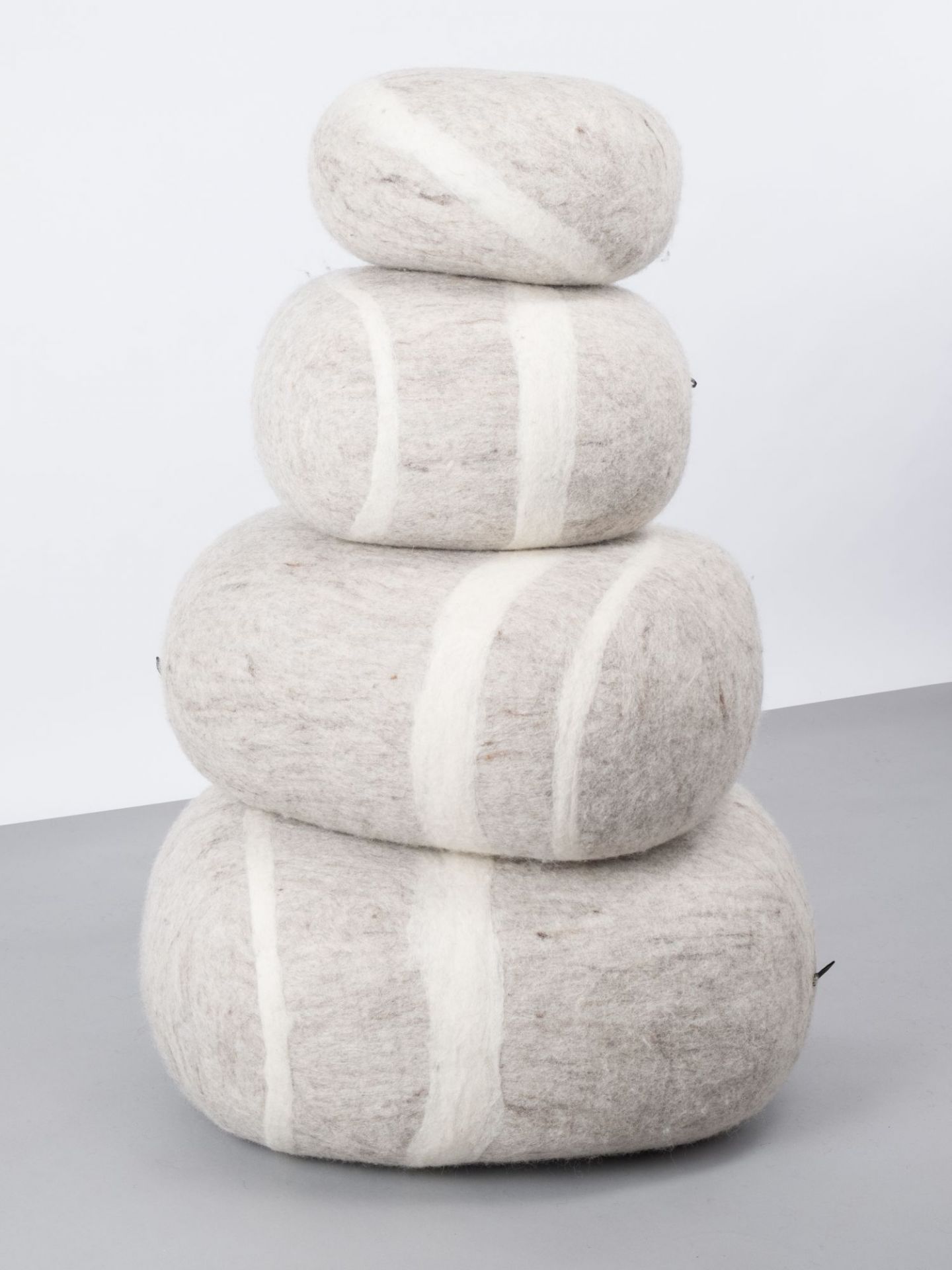 Filz Kieselstein Hocker Béla: Vier gestapelte, graue Filzkissen mit weißen Streifen als Sitzgelegenheit.