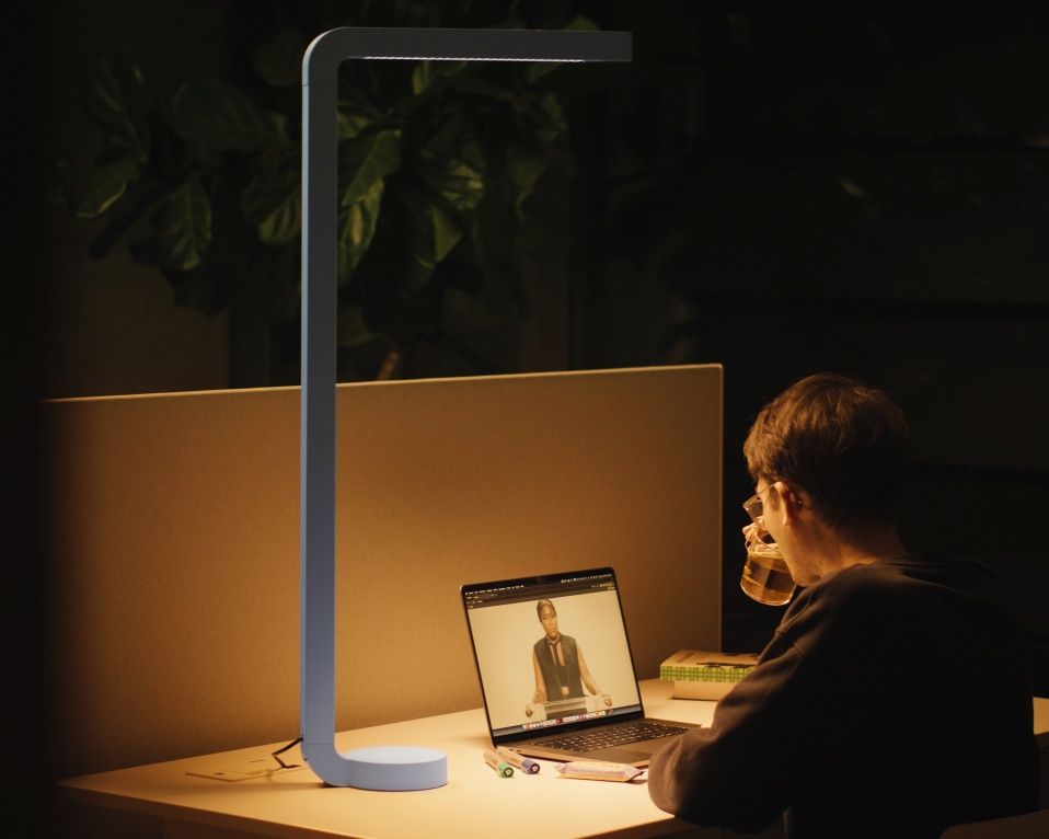 Graue Team Home Tischleuchte beleuchtet Schreibtisch mit Laptop und Person bei Online-Meeting. Moderne LED-Tischlampe für Büro.