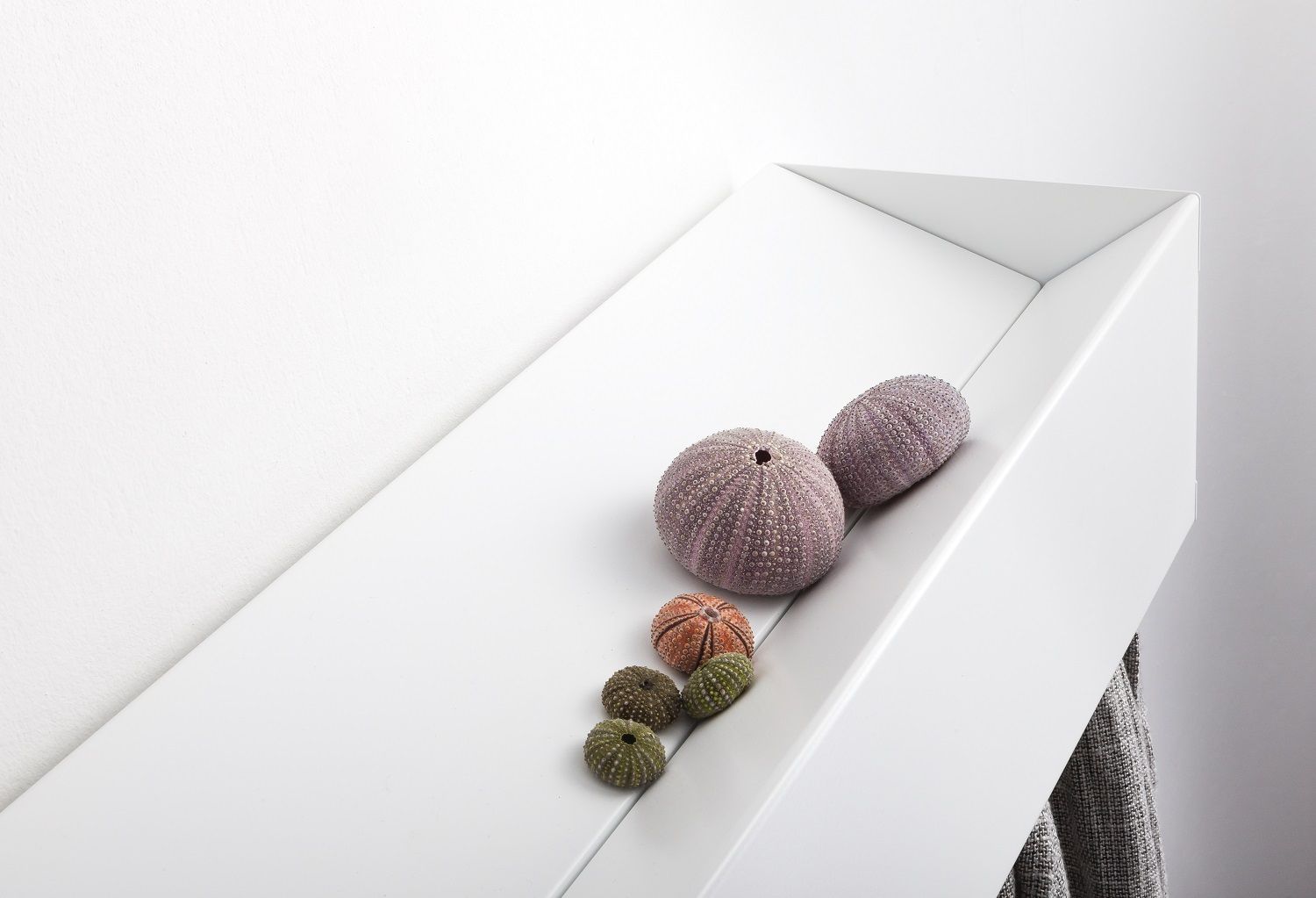 Weiße Wandgarderobe CR Linea1 von Müller Möbelwerkstätten mit dekorativen Seeigeln und Handtuch, minimalistisches Design.