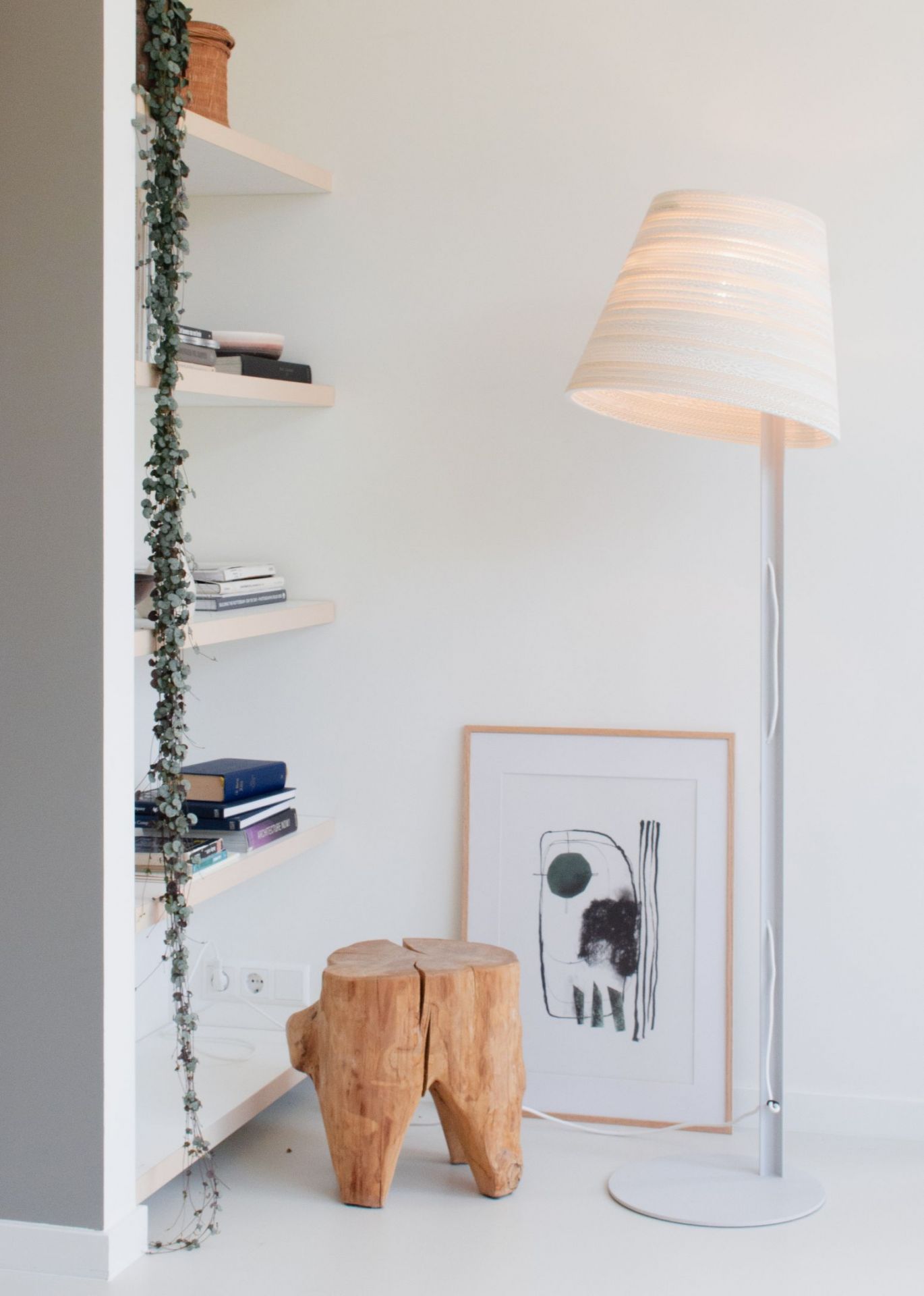 Weiße Tilt Stehleuchte Scraplights von Graypants im minimalistischen Wohnzimmer mit Holzschemel und Kunstwerk.