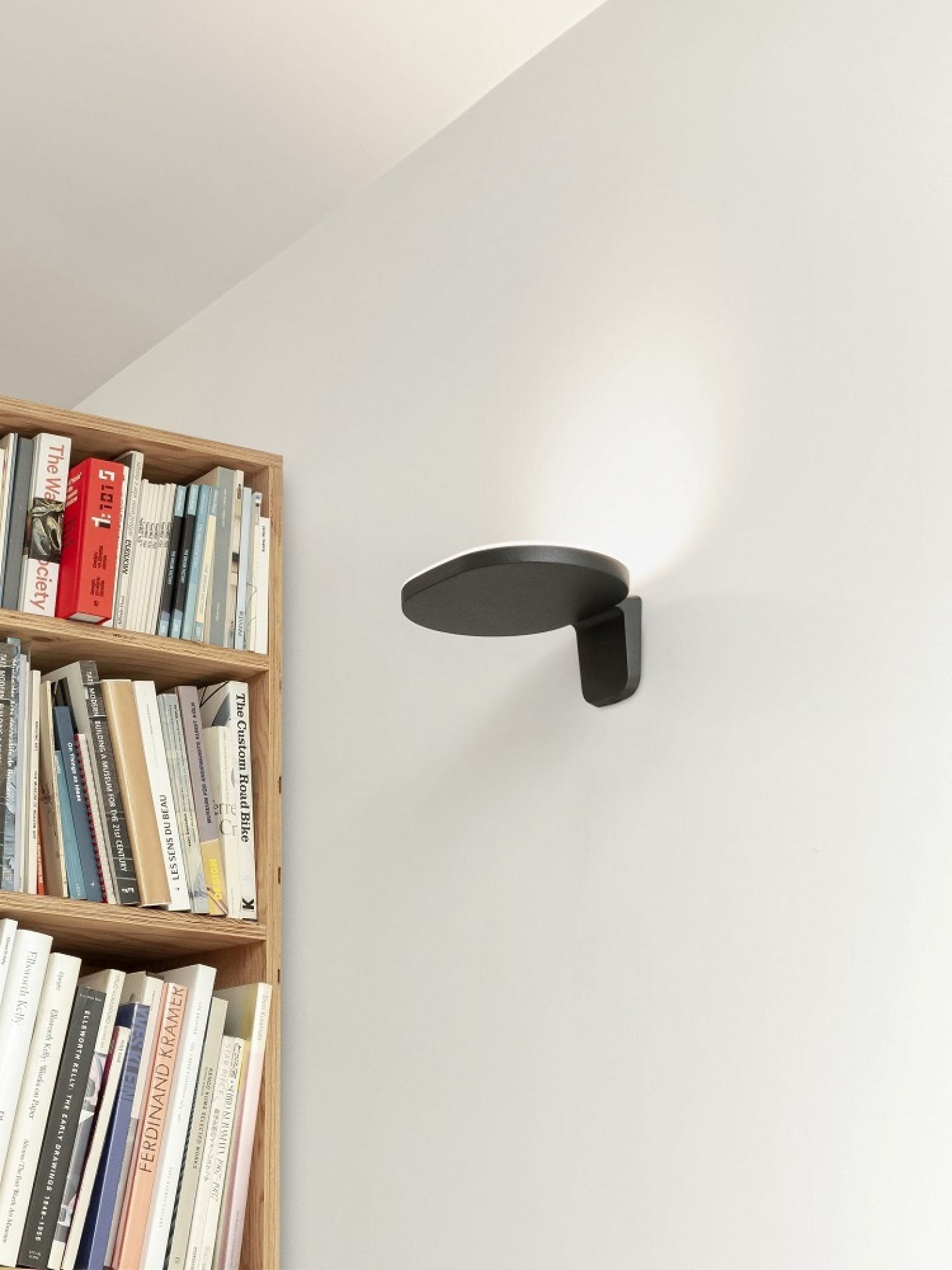 Oplight W1 Wandleuchte von Flos, weiße Wandlampe neben Bücherregal, modernes Design, indirekte Beleuchtung.