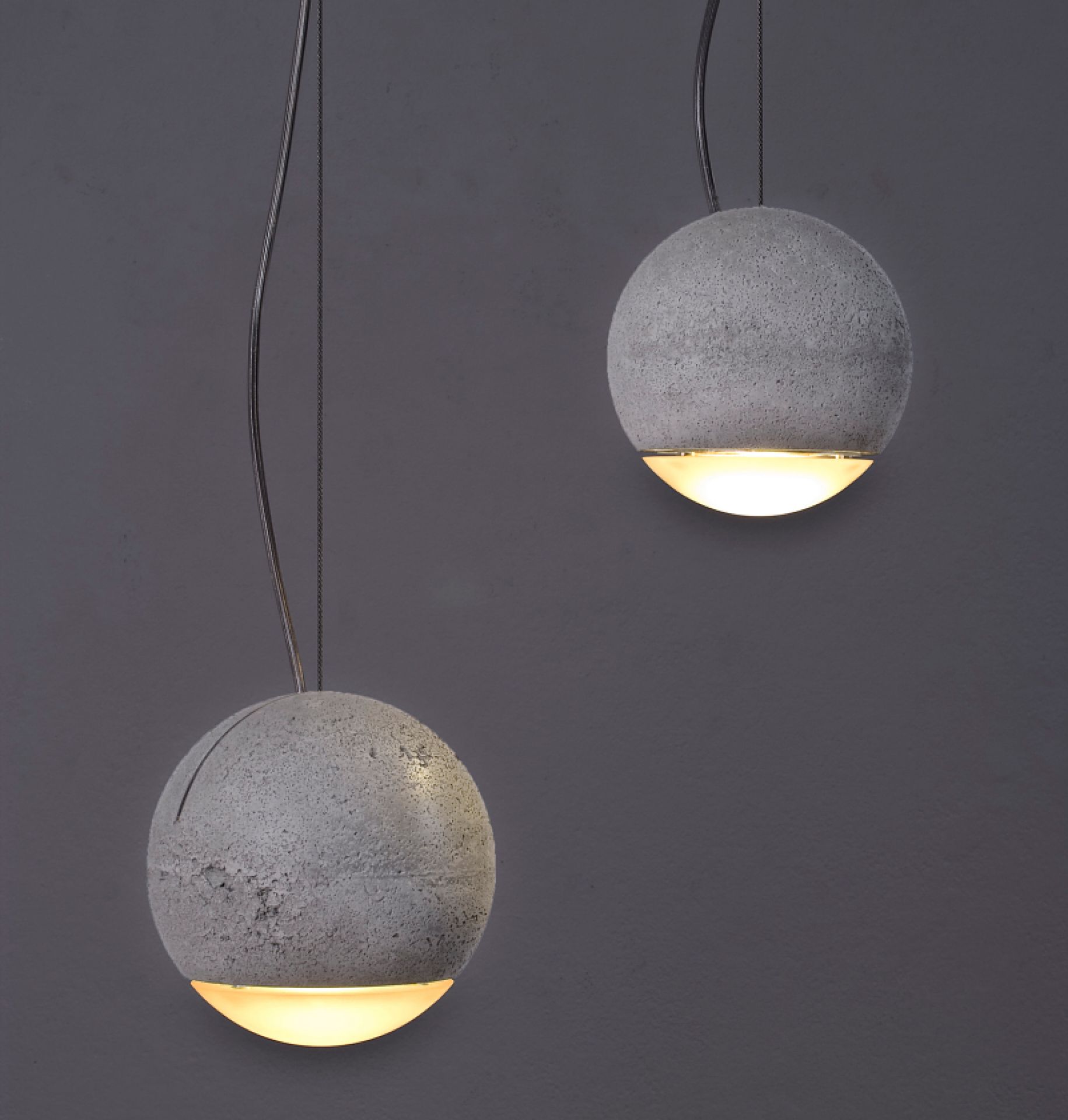 Zwei Trabant 2 Pendelleuchten von Tecnolumen, kugelförmig aus Beton, mit warmweißem Licht nach unten.
