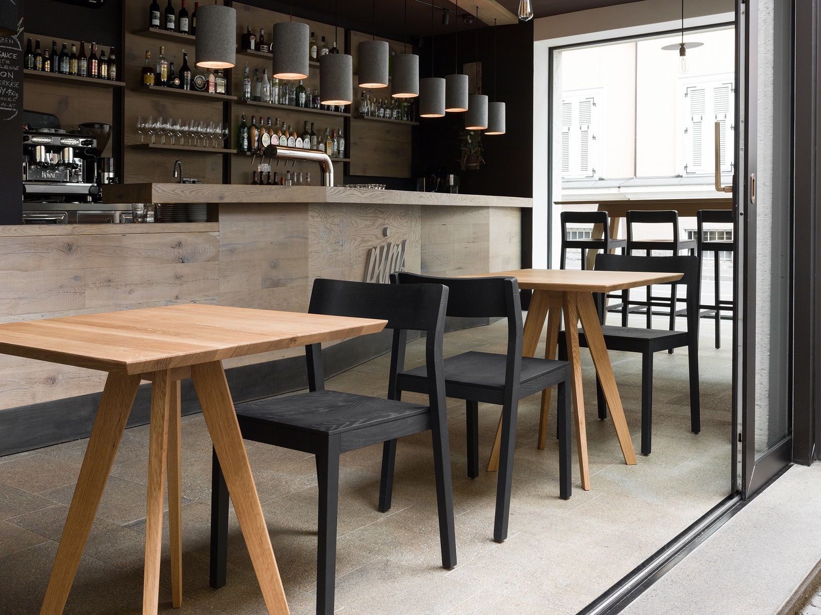 Quadratischer CENA Tisch aus Holz mit passenden Stühlen in einem modernen Restaurant.