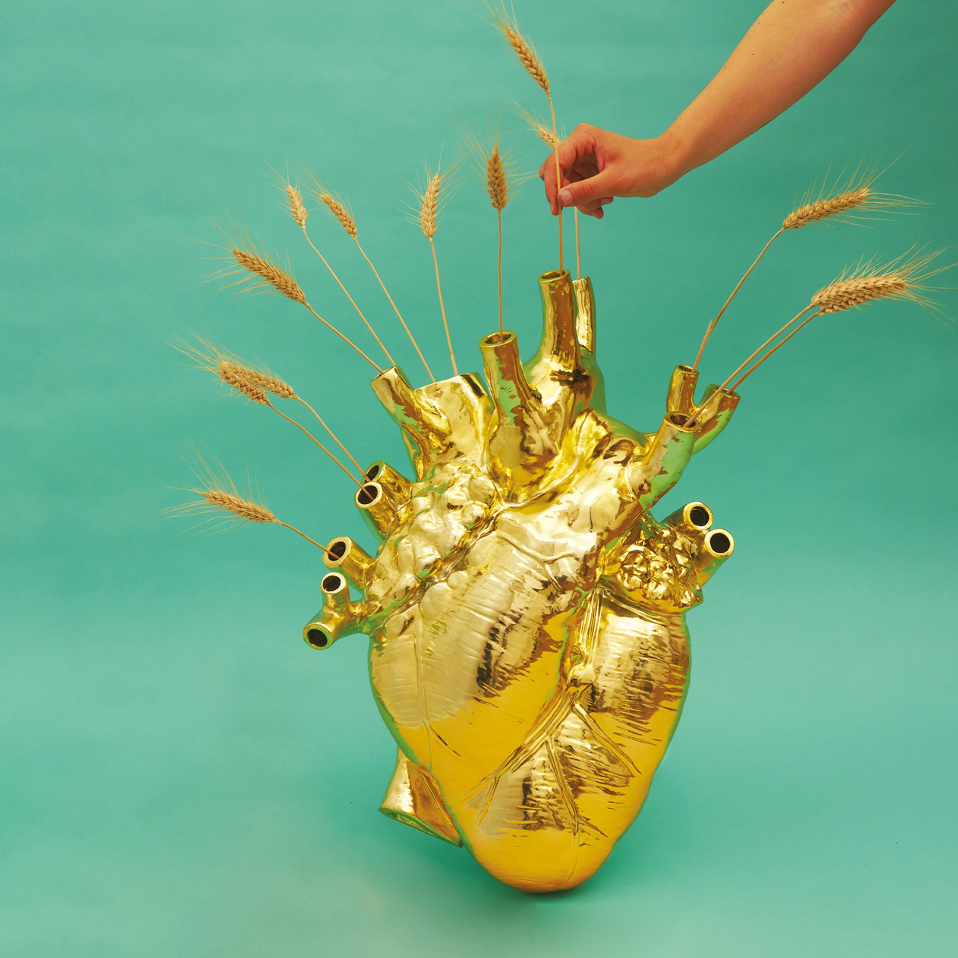 Goldene Love in Bloom Herz-Vase von Seletti mit Weizenähren auf türkisfarbenem Hintergrund. Dekorative Design-Vase.