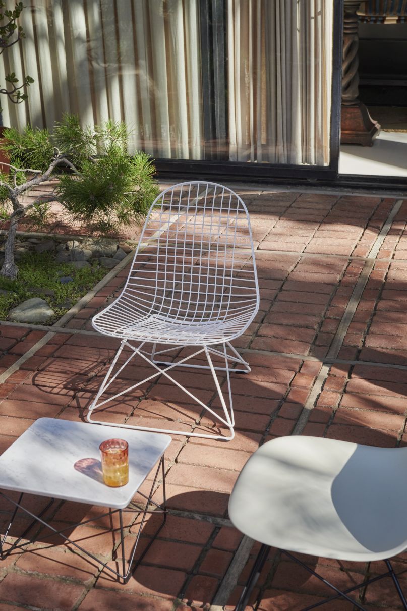 Weißer Eames Stuhl mit Drahtgestell von Vitra auf einer Terrasse, modernes Design.
