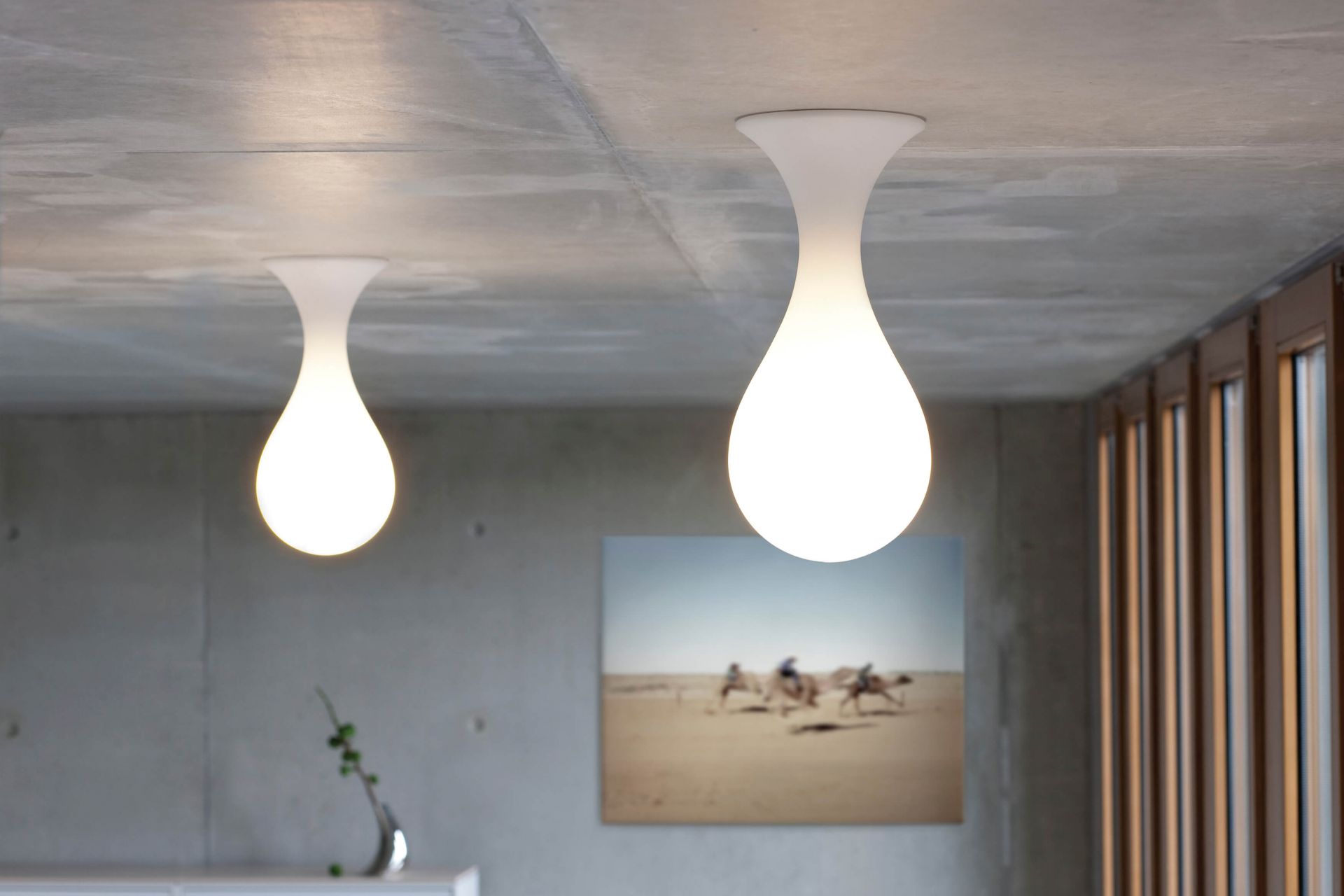 Zwei Liquid Light Deckenleuchten, tropfenförmig, in modernem Interieur mit Betonwand und Fenster.