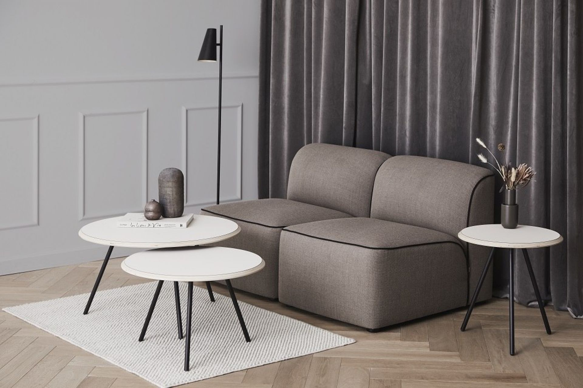 Wohnzimmer-Szene mit Cono Stehleuchte von Woud, grauem Sofa und weißen Beistelltischen.