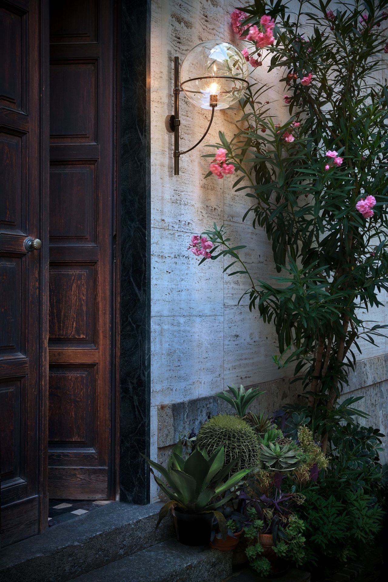 Lyndon Außenwandleuchte mit Glaskugel und floraler Dekoration neben einer dunklen Holztür.