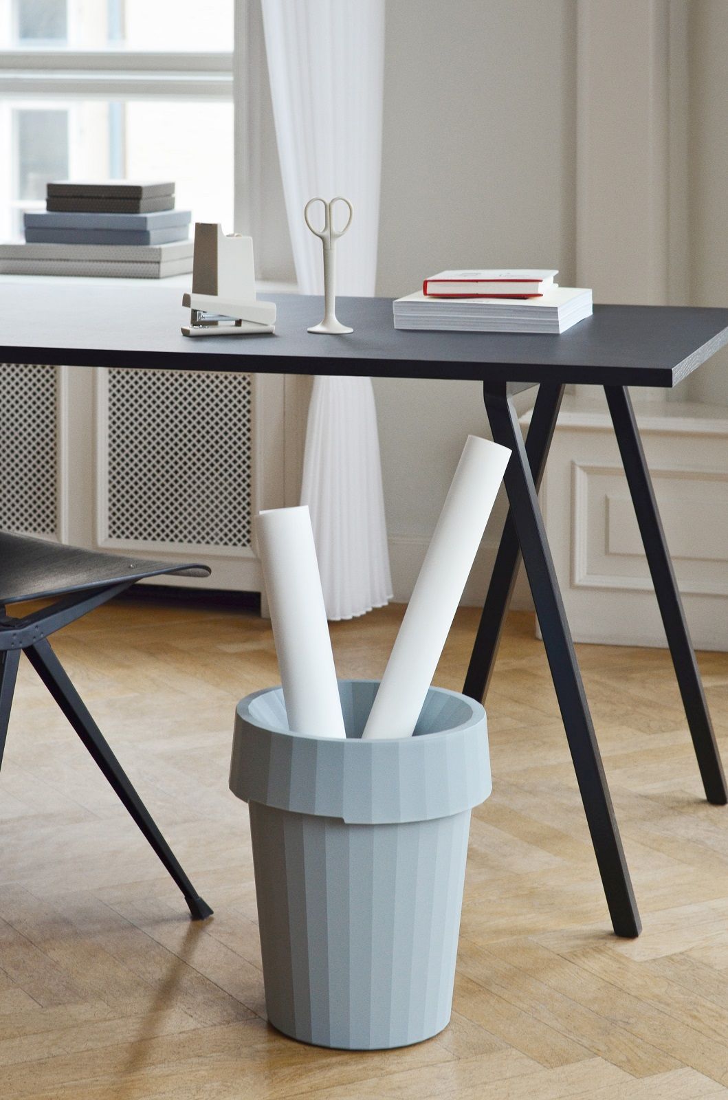 Schwarzer Loop Stand Table von Hay mit Büromaterialien und hellblauem Papierkorb im minimalistischen Interieur.
