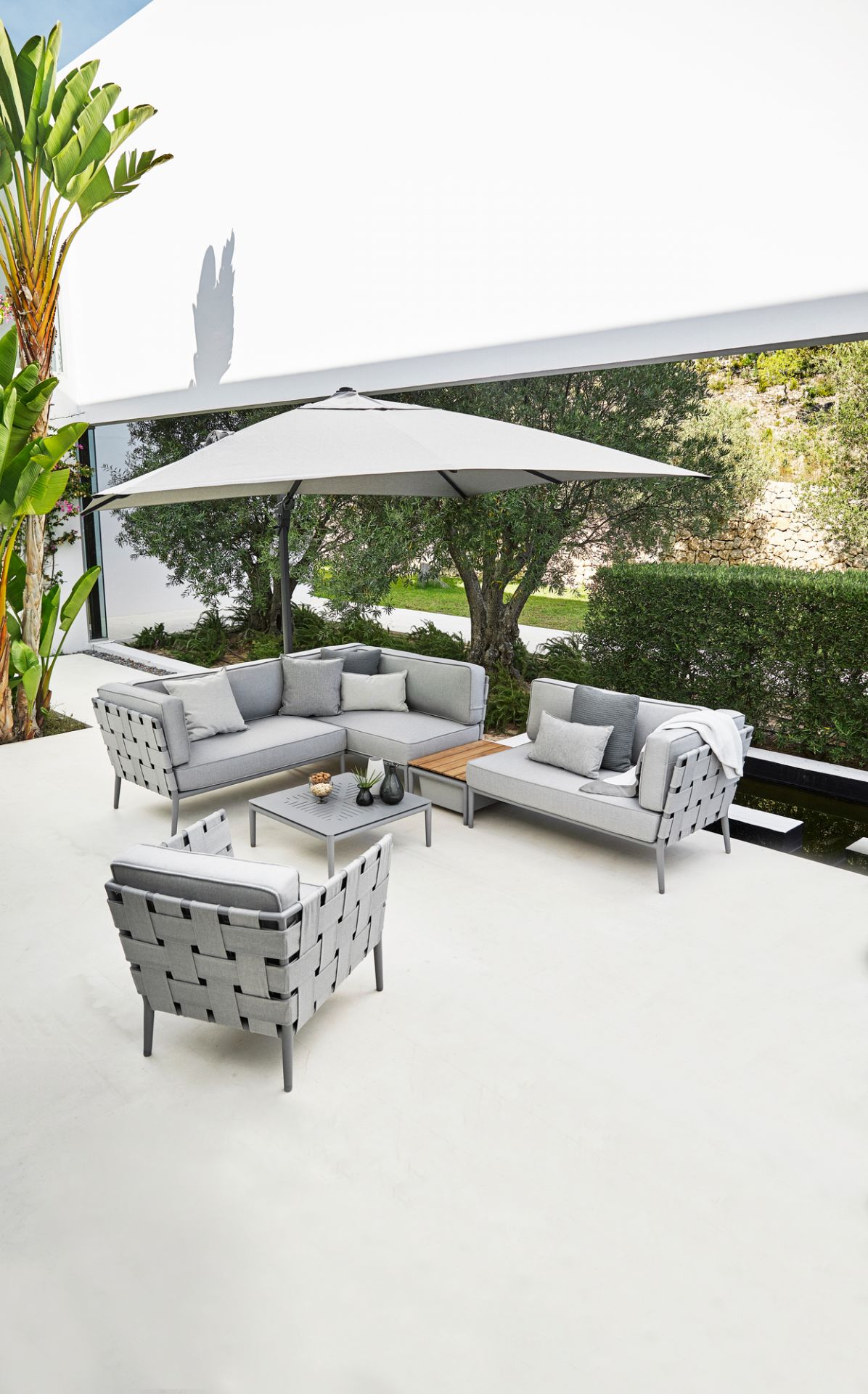 Heller Conic AirTouch Loungesessel von Cane-Line im Outdoor-Bereich mit Lounge-Möbeln und Sonnenschirm.