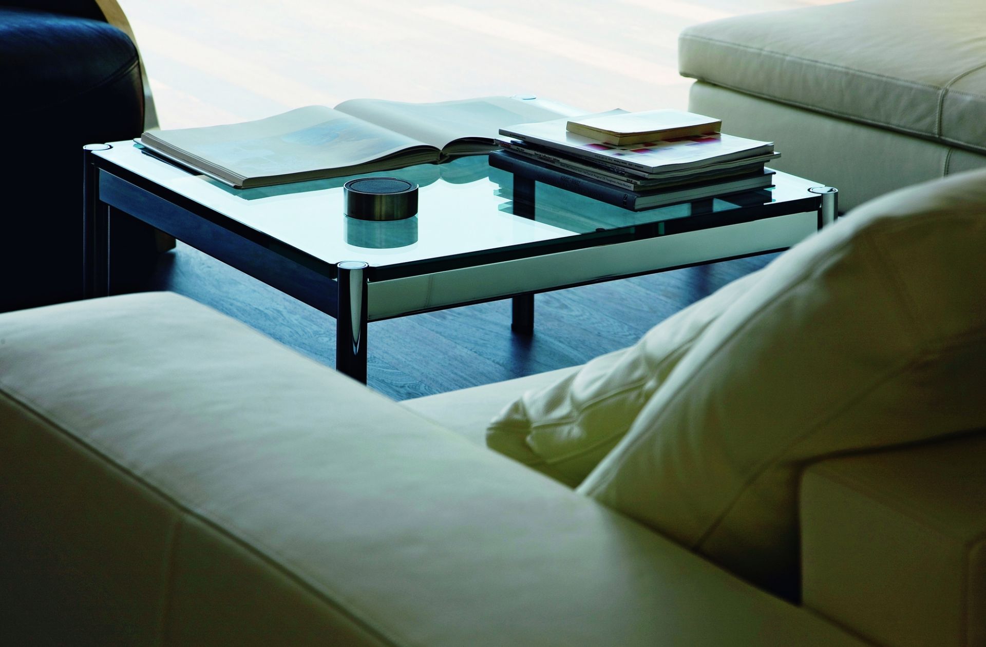 USM Haller Couchtisch 75x75 cm mit Glasplatte, Magazinen und stilvollem Design neben einem beigen Sofa.