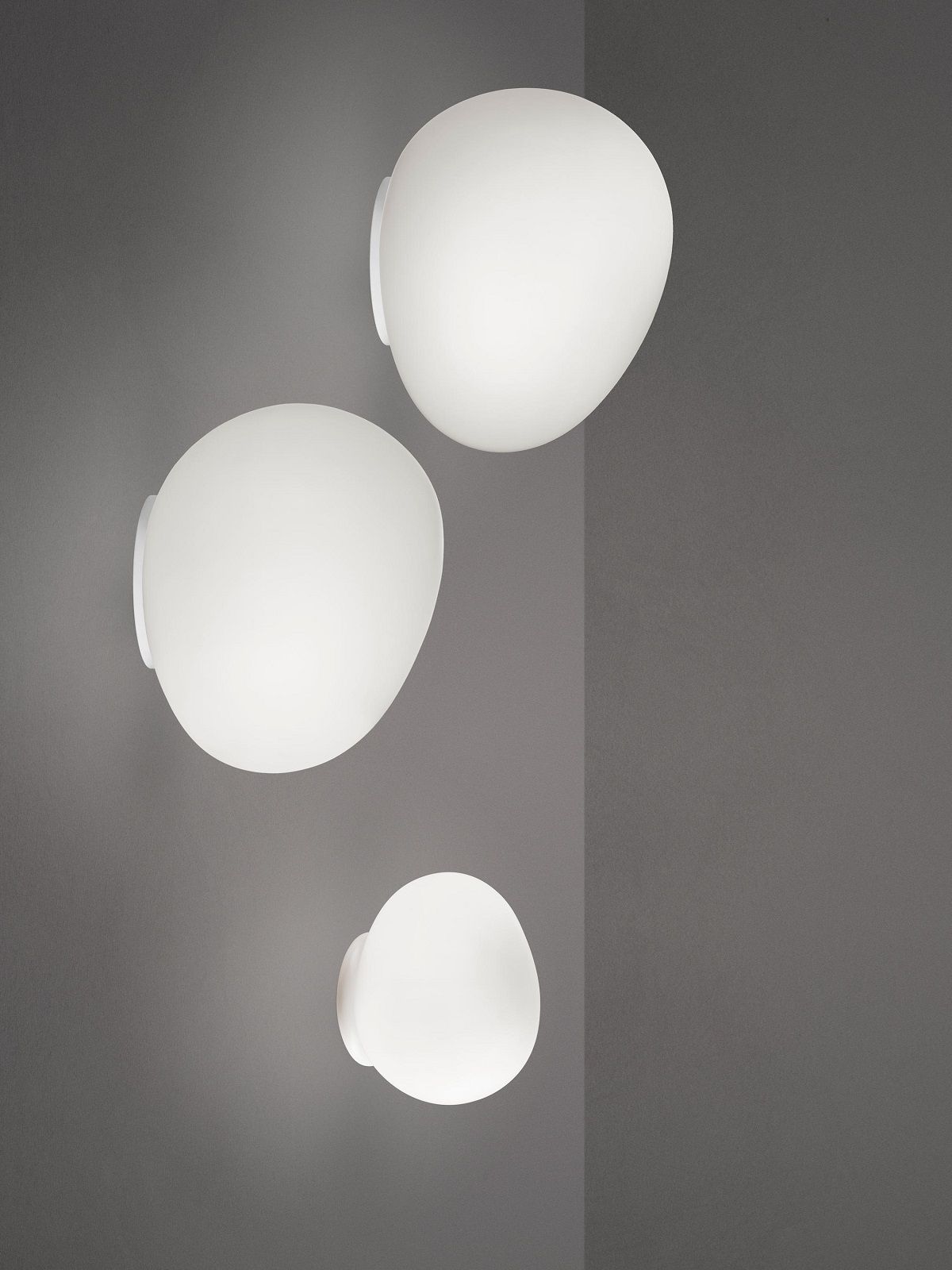 Drei weiße Gregg Wandleuchten von Foscarini an einer grauen Wand, modernes Design.