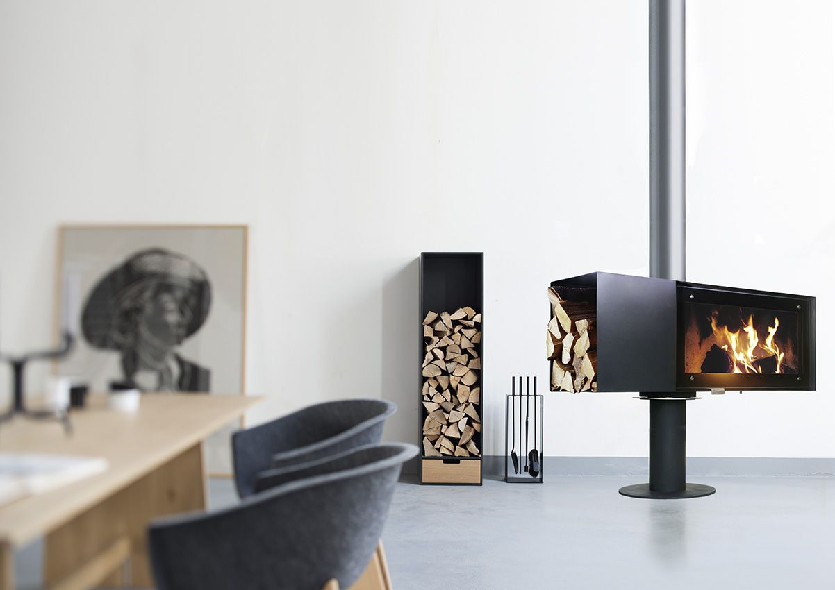 Covo Brennholzregal von Conmoto neben Kaminofen mit Holz und Kaminbesteck im modernen Wohnraum.