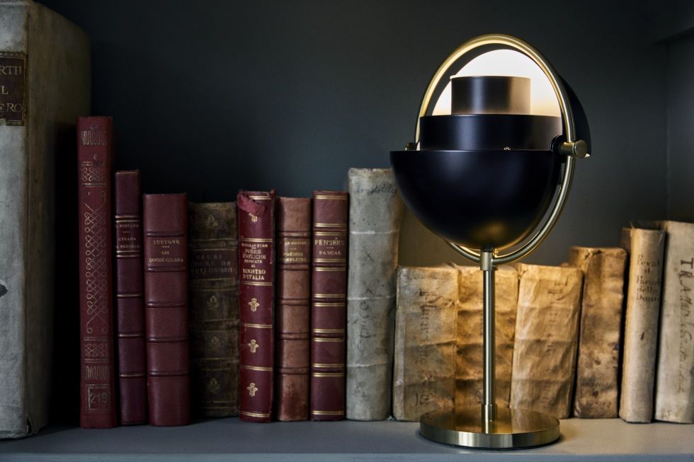 Gubi Multi-Lite Portable Lamp Akkuleuchte in Schwarz und Gold zwischen alten Büchern.