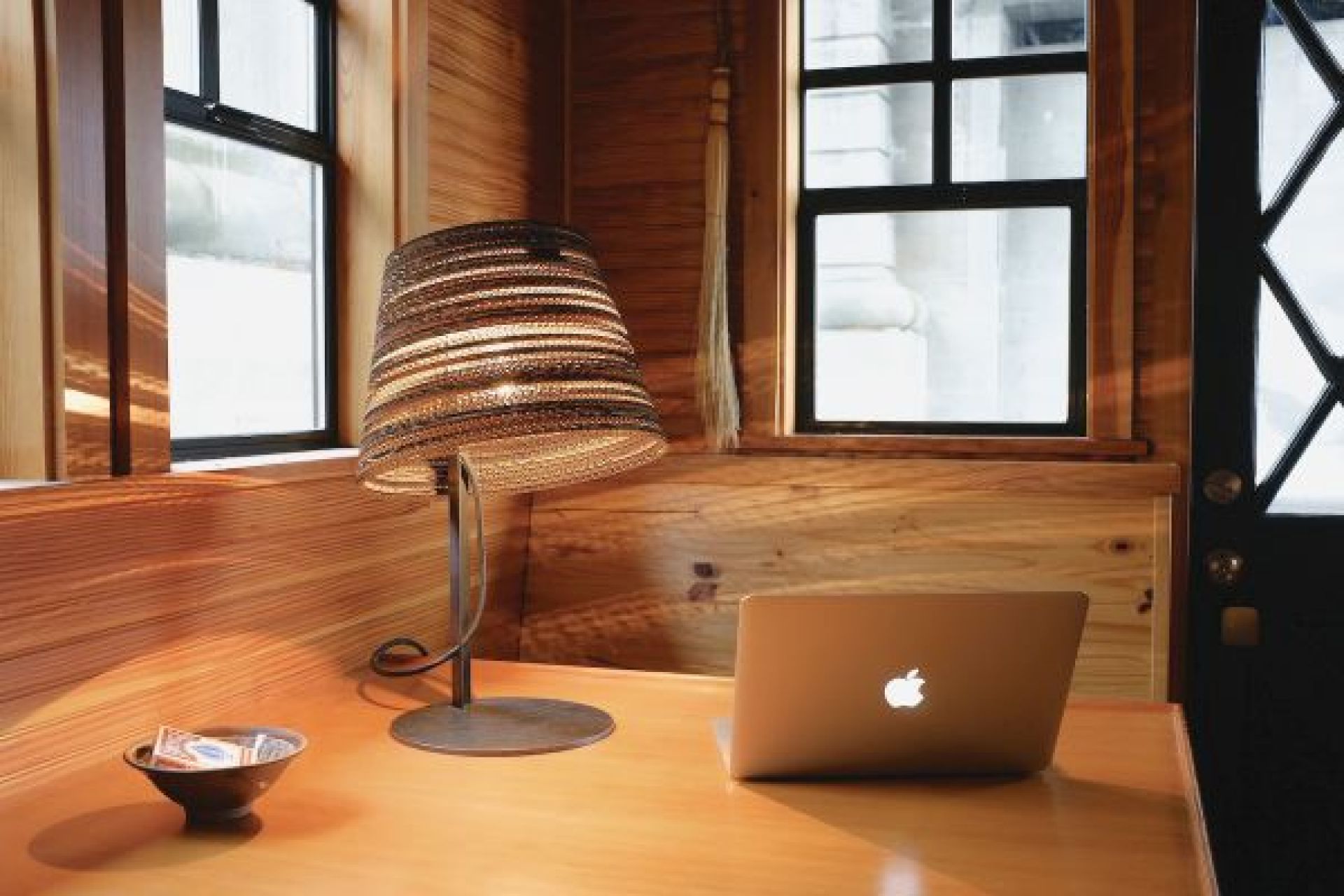 Tilt Tischlampe Scraplights Graypants aus recycelter Pappe auf einem Holztisch neben einem Laptop.