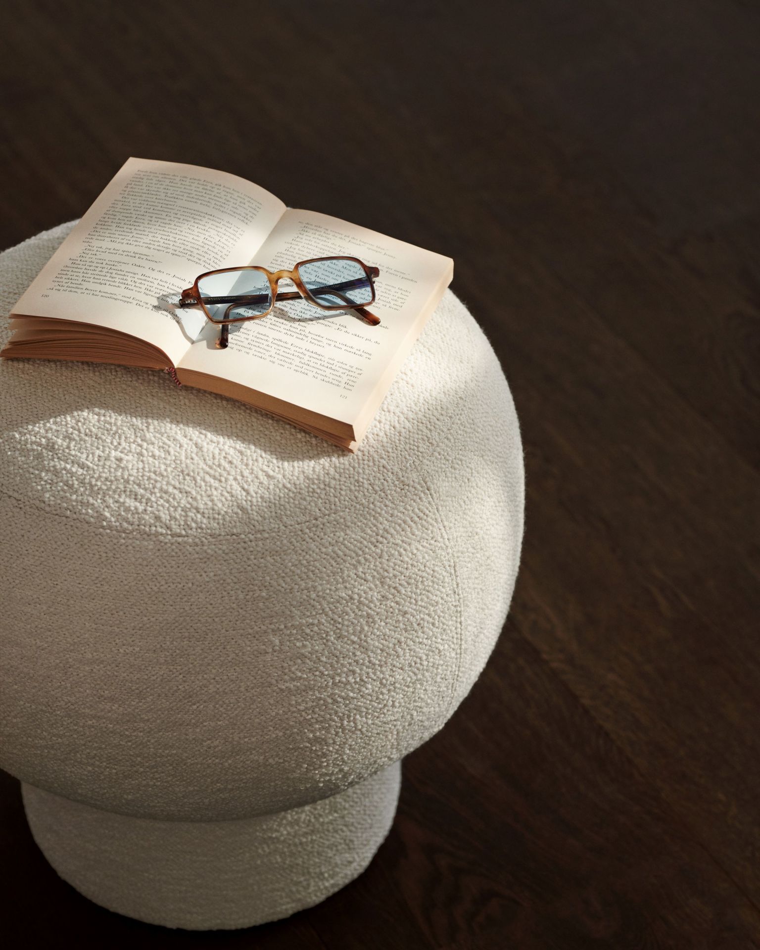 Weißer Liége Pouf von Norr11 mit Buch und Brille für gemütliche Lesestunden.