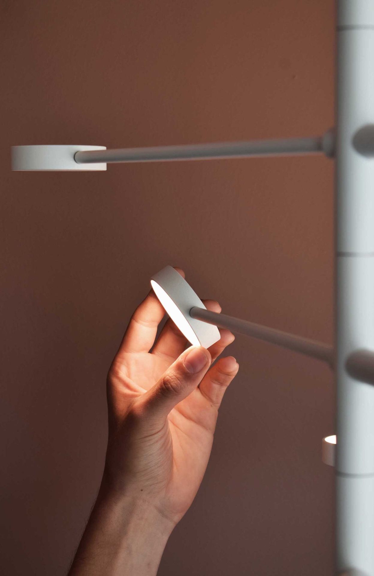 Hand hält KINGPIN Pendelleuchte Japth, modernes Design, minimalistische Hängelampe, warmes Licht.