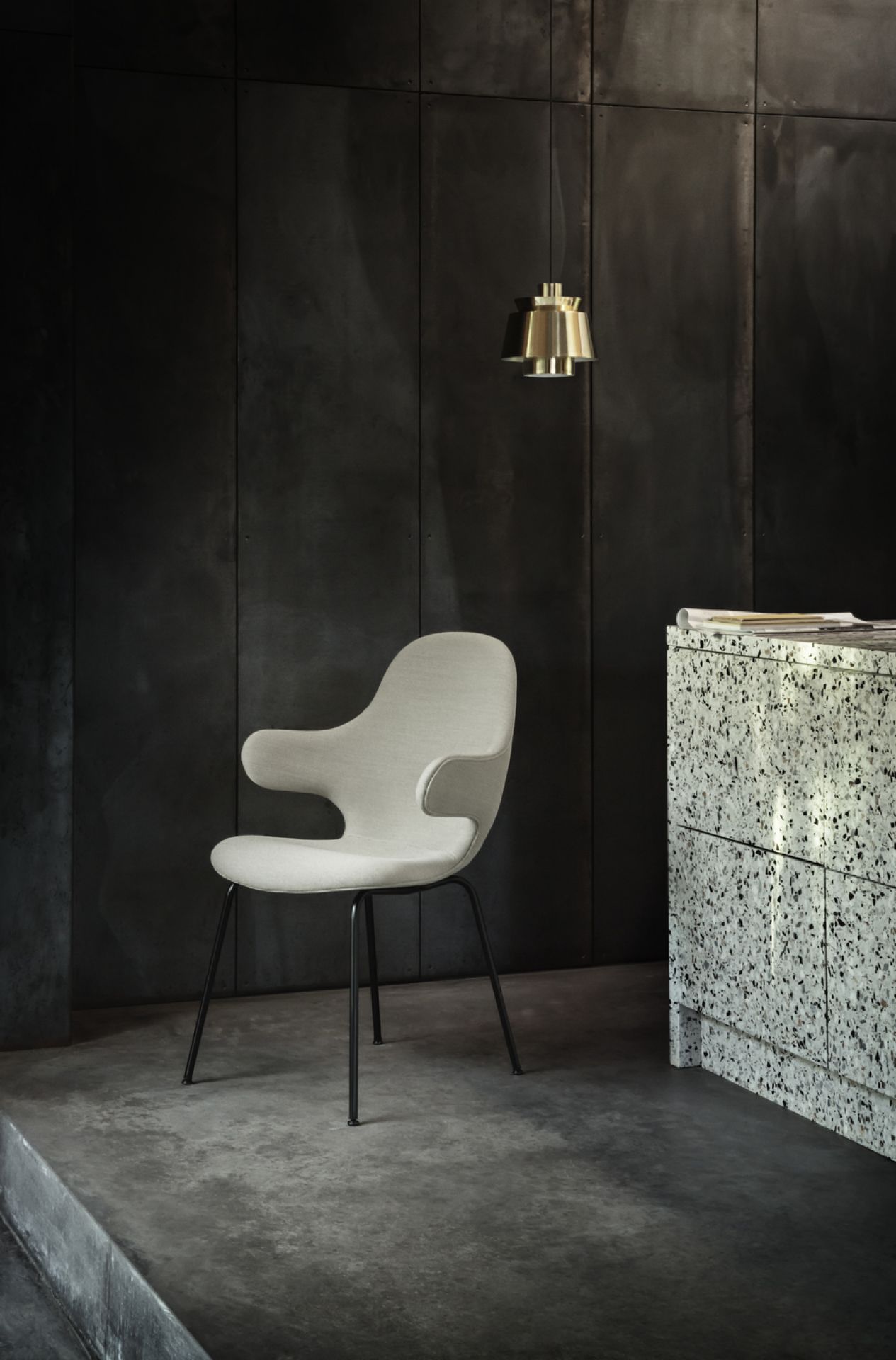 Nahaufnahme der AndTradition Utzon JU1 Pendelleuchte aus Messing über einem modernen Stuhl und Schrank.