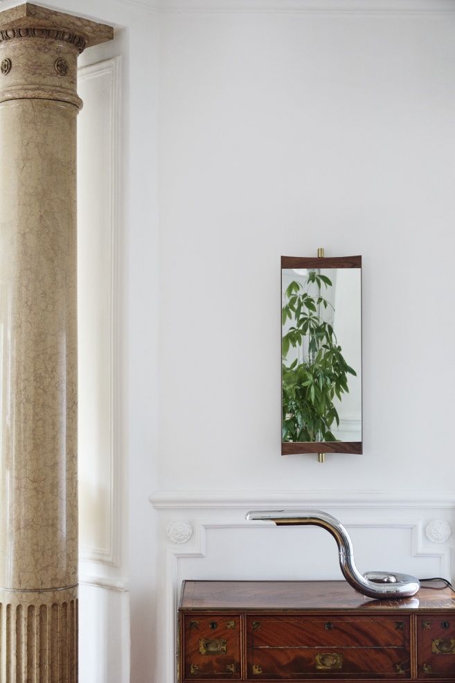 Gubi Vanity Wandspiegel mit Holzrahmen und Messingdetails an weißer Wand über Kommode.