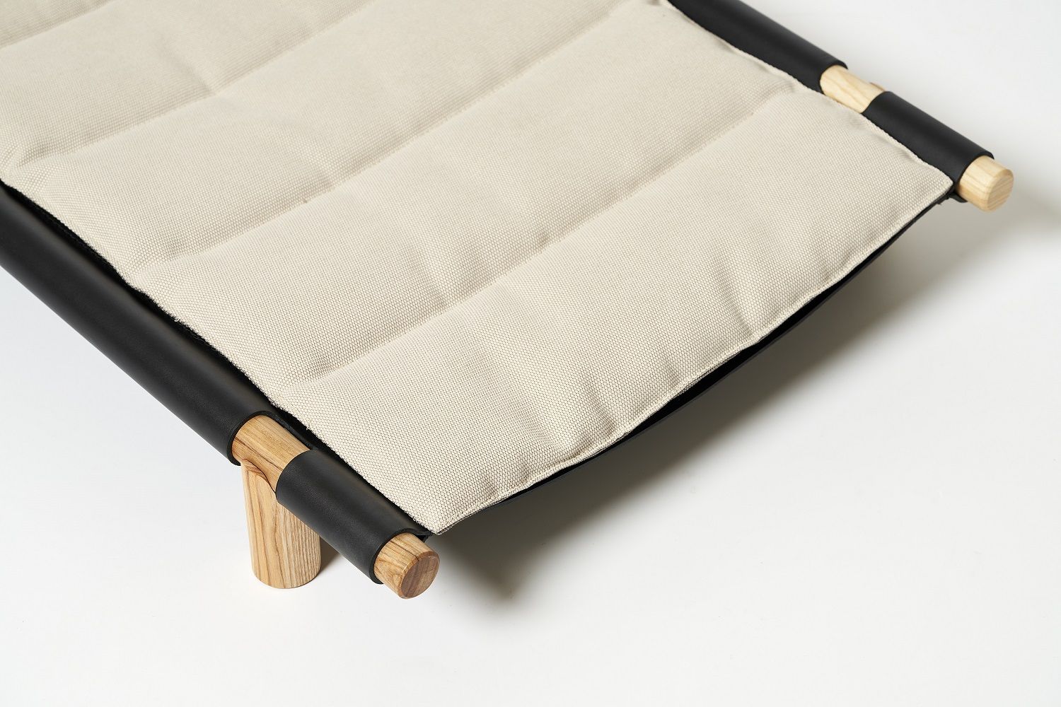 Detailaufnahme: Berberé Hundebett tragbar von Opinion Ciatti mit gesteppter, beiger Liegefläche und Holzgestell.