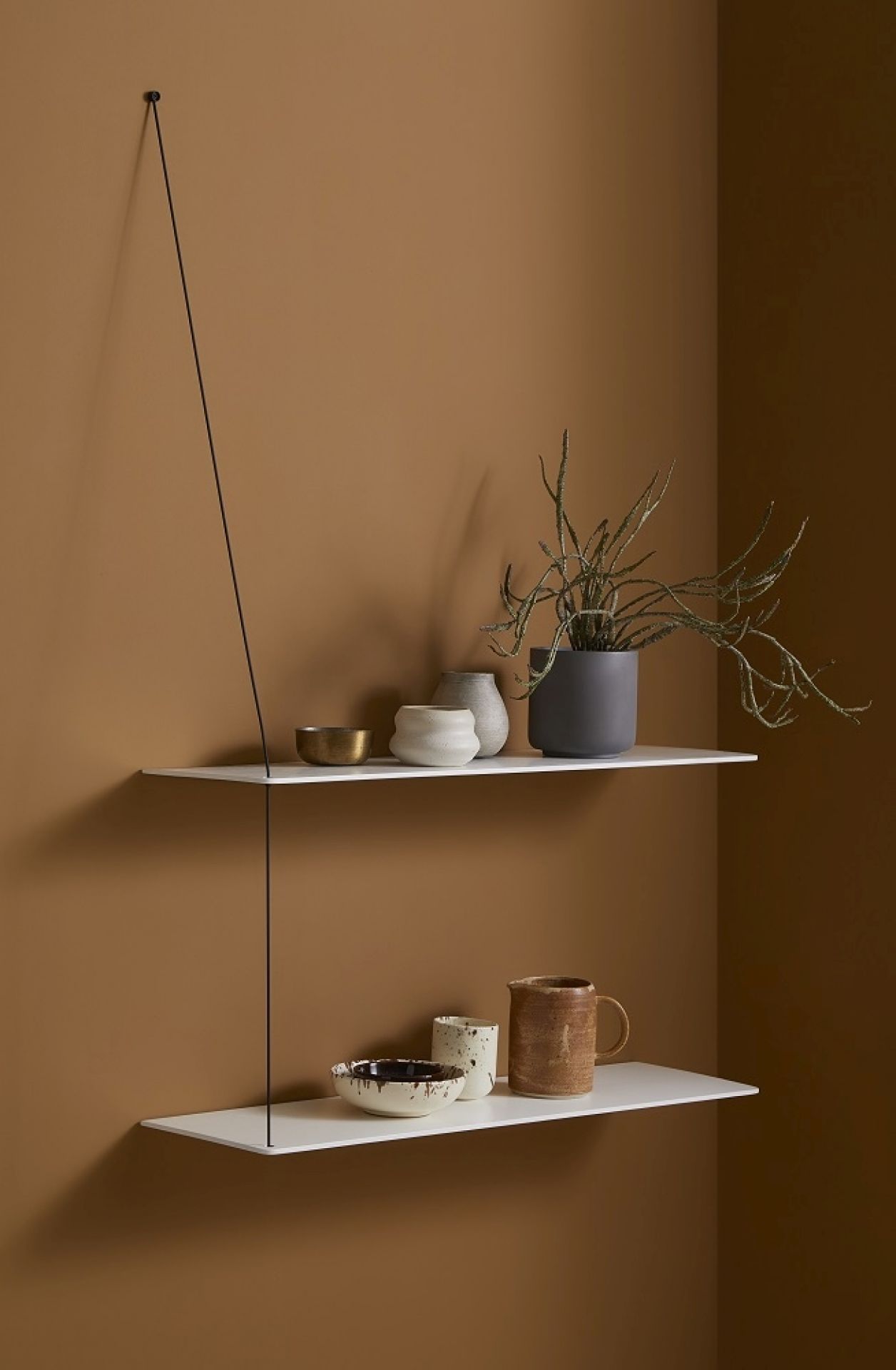 Weißes Stedge Add-on Wandregal von Woud mit Deko-Objekten vor brauner Wand.