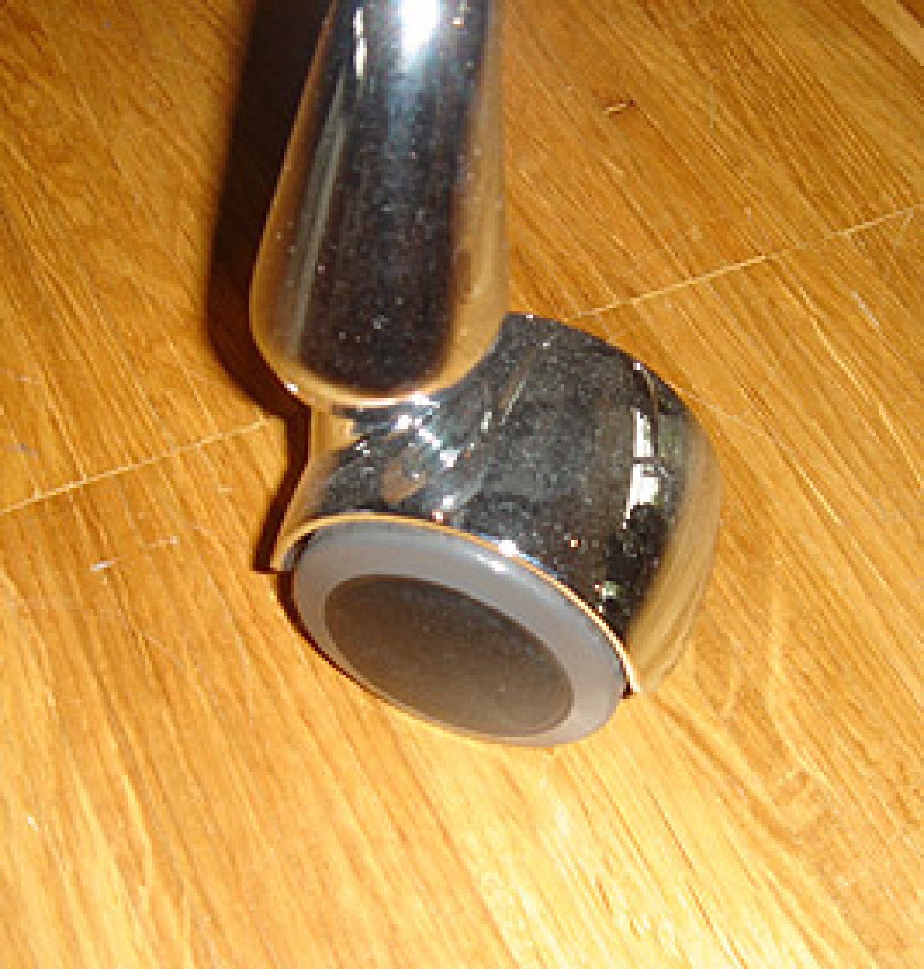 Nahaufnahme einer verchromten Vitra Drehstuhlrolle für Eames Aluminium Chair auf einem Holzboden.