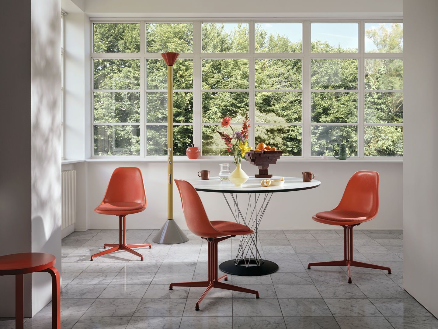 Esszimmer mit drei roten Eames La Fonda Stühlen und rundem Tisch. Vitra Designklassiker.