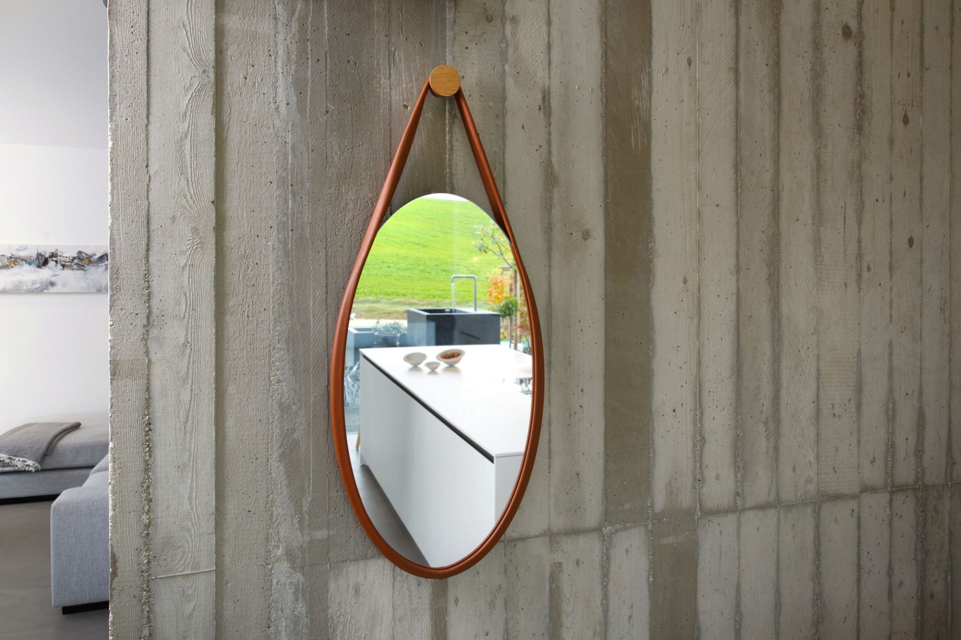 Favius Wandspiegel mit braunem Rahmen und Eichenholzaufhängung vor Betonwand. Design Spiegel für Wohnraum.