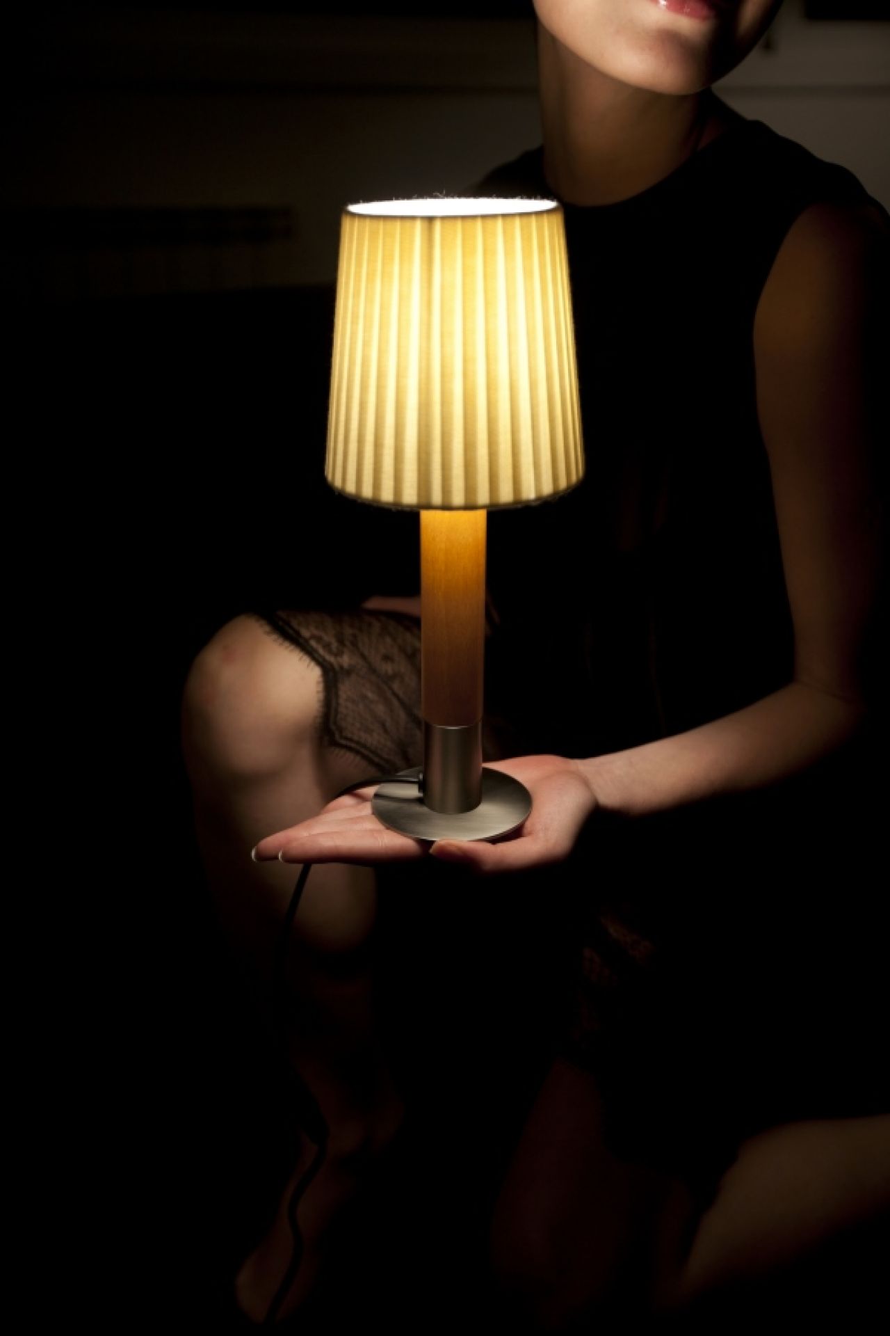 Frau hält beleuchtete Basica Tischleuchte von Santa & Cole mit plissiertem Schirm.