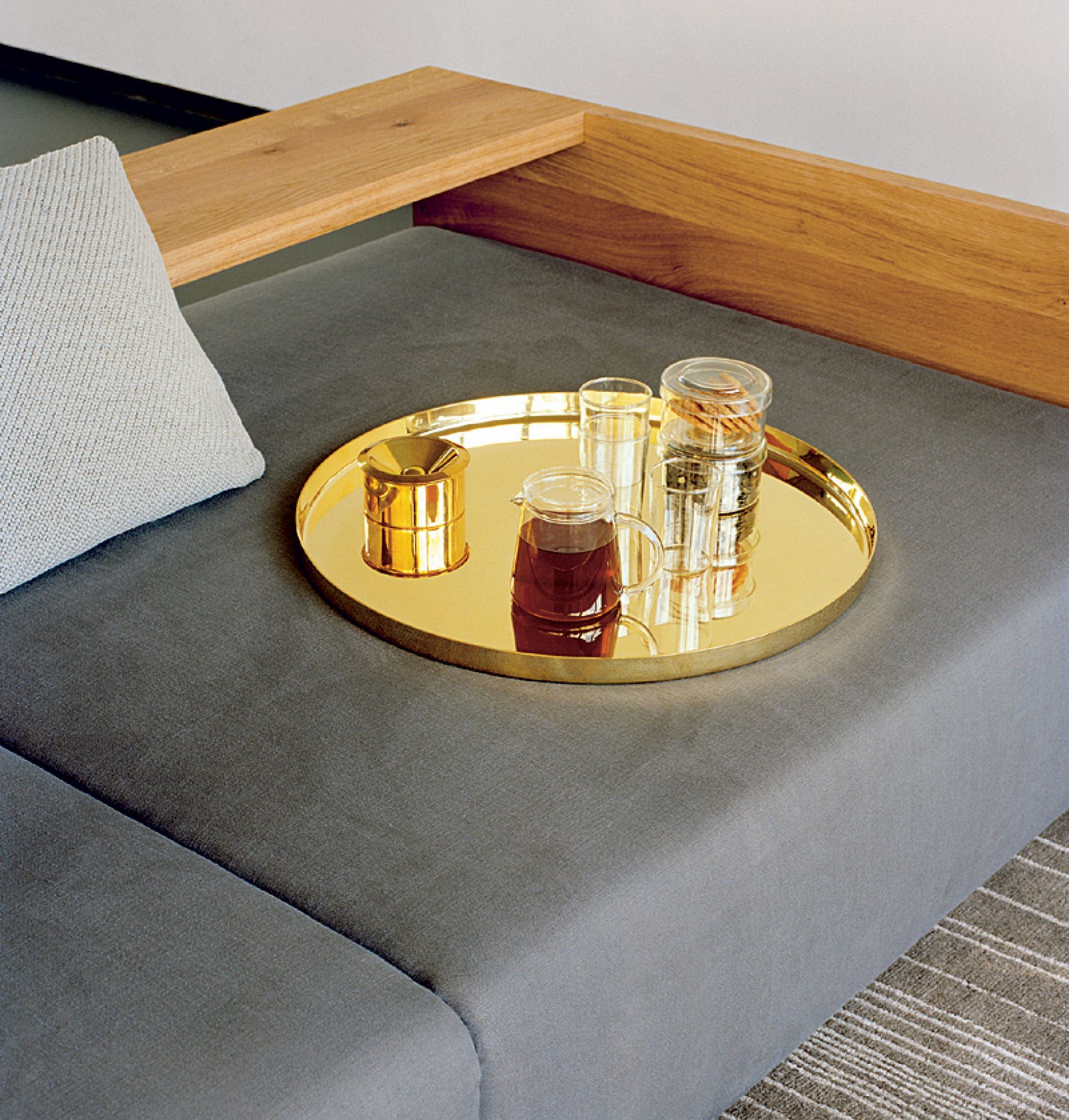 Goldenes Habibi Tablett von e15 mit Teekanne und Gläsern auf einem grauen Sofa.