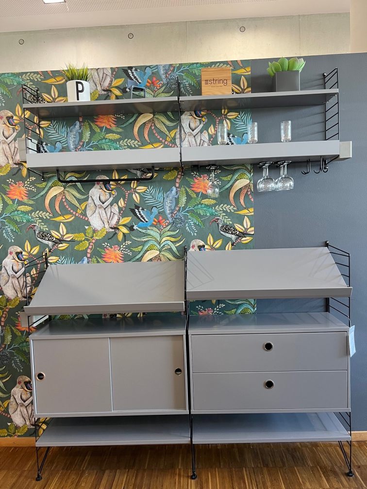 Graues String Regal mit Schränken und Regalböden vor gemusterter Tapete, String Furniture Ausstellung.