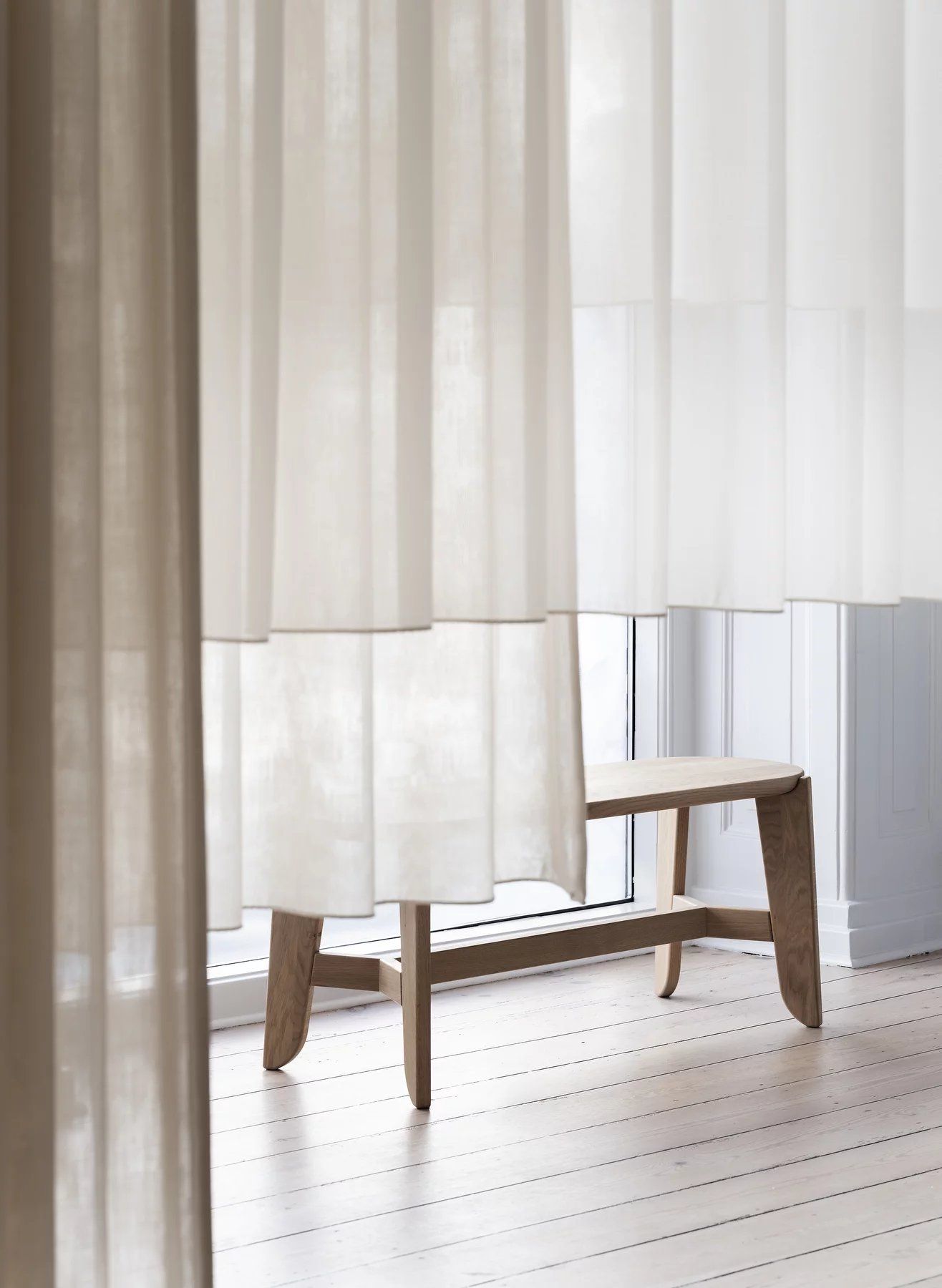 Heller Holz-Barhocker, Blomus Eli Bar Stool, vor einem Fenster mit Vorhängen. Modernes Möbeldesign.