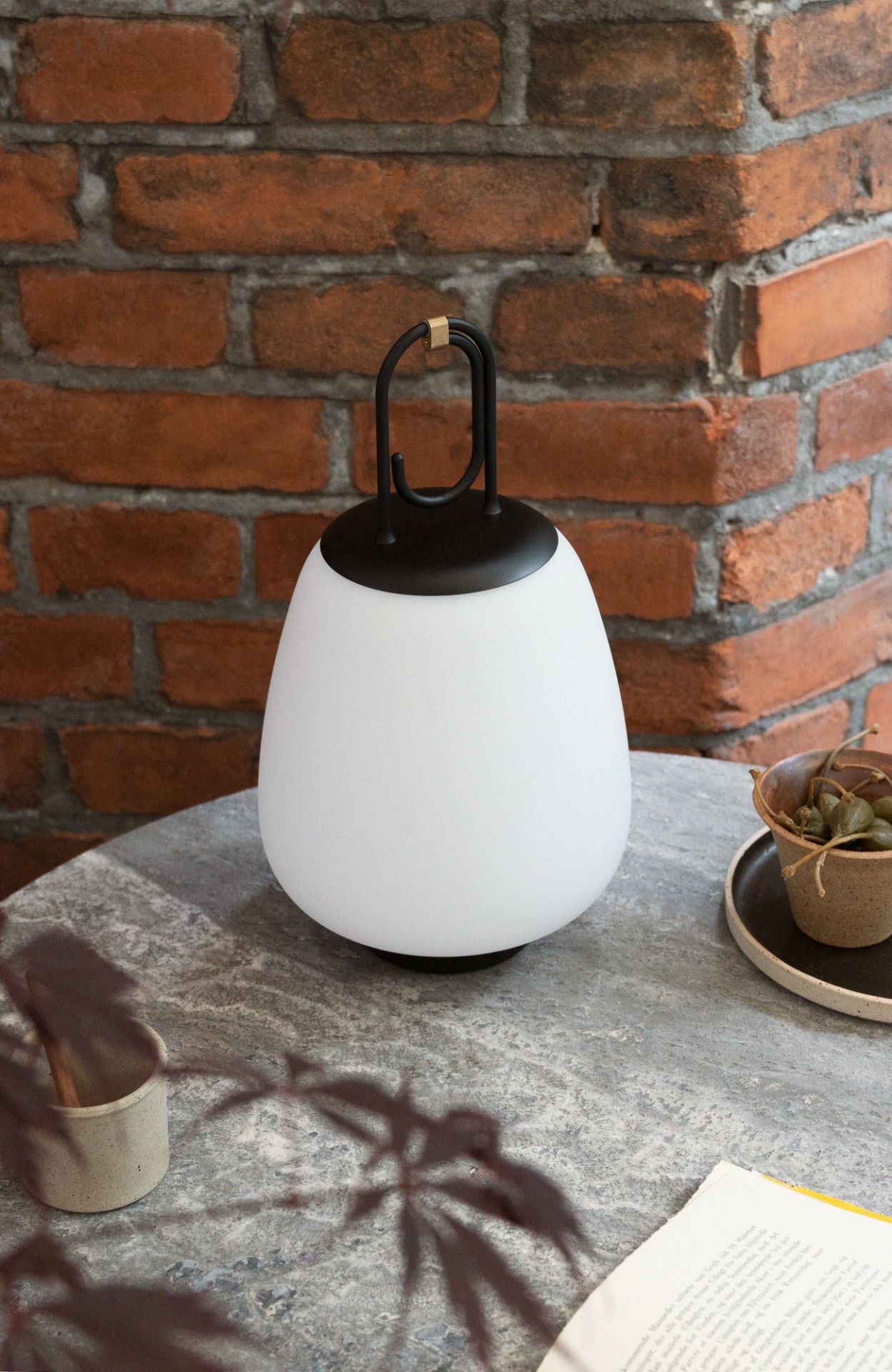 Schwarze Lucca Akkuleuchte von AndTradition auf Tisch, geeignet für drinnen und draußen.