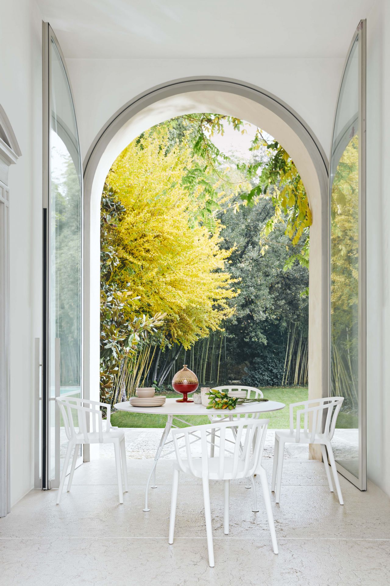 Runder, weißer Esstisch von Kartell mit Marmor-Optik und vier weißen Stühlen im Garten.