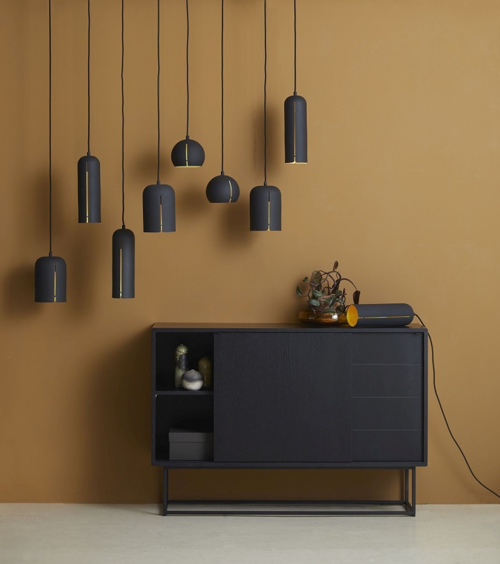 Mehrere Gap Pendelleuchten von Woud, runde Hängelampen in Schwarz mit goldenen Akzenten über einem Sideboard.