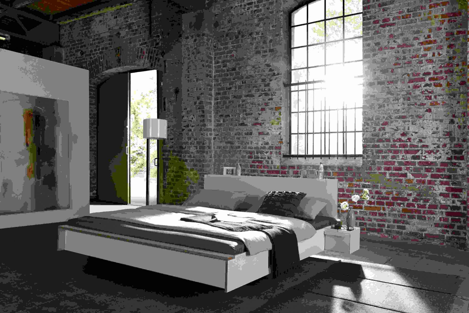 Weißes Flai Bett Kopfteil von Müller Möbelwerkstätten im Schlafzimmer mit Backsteinwand und großem Fenster.