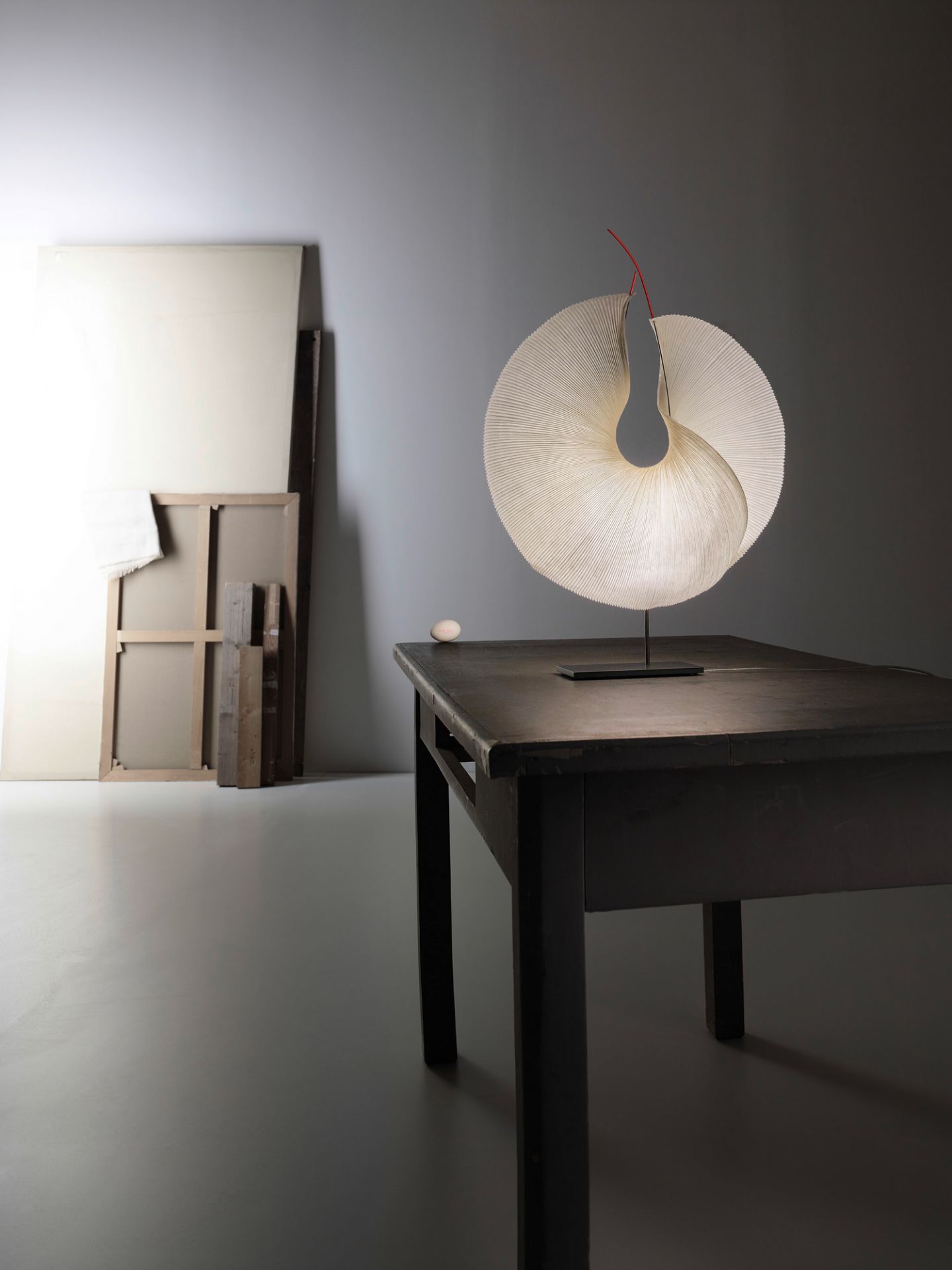 Yoruba Rose Tischleuchte von Ingo Maurer, Design Lampe mit plissiertem Lampenschirm und rotem Detail.