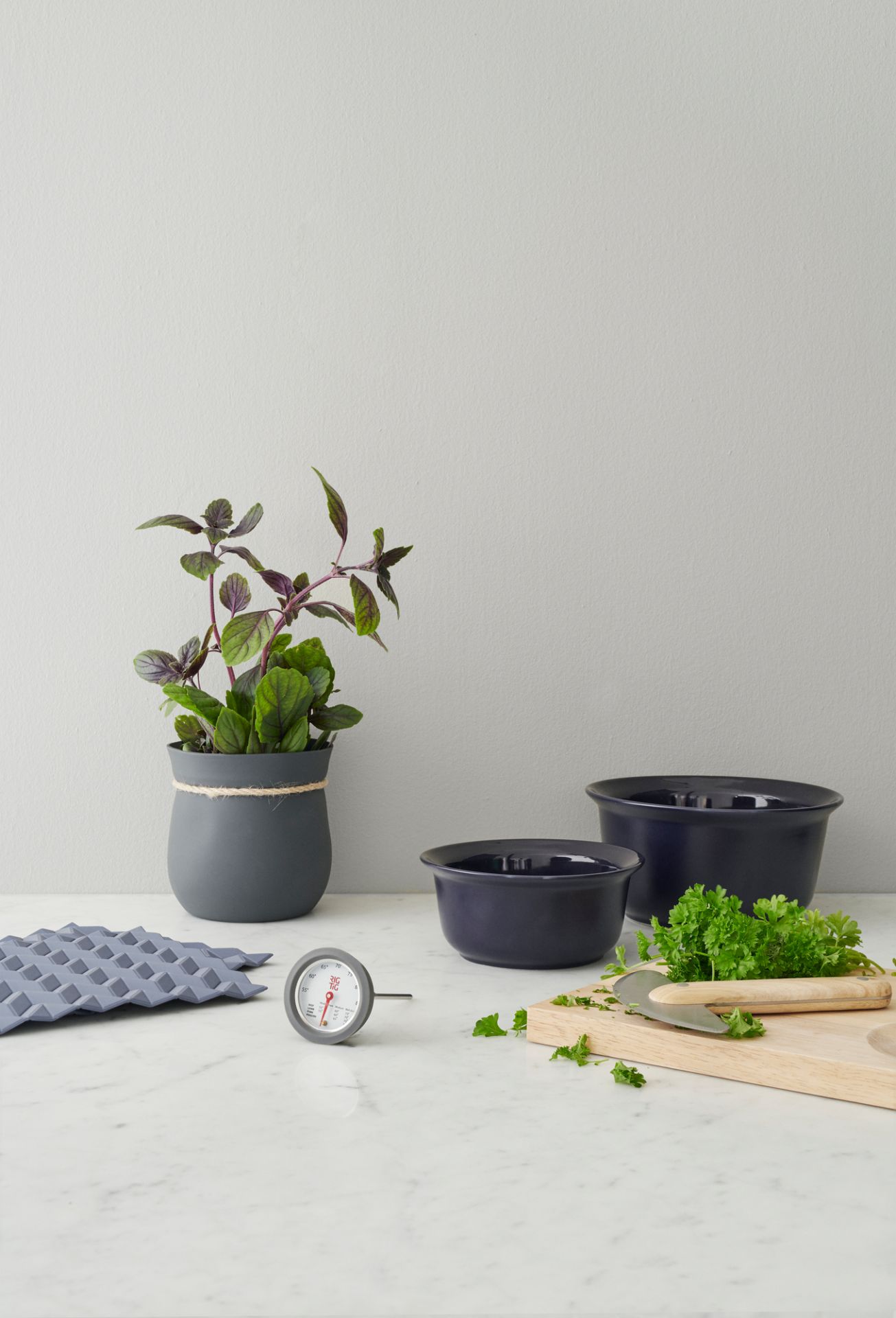 Blauer Hold-On Topflappen von RIG-TIG by Stelton neben Kochutensilien und Kräutern auf einer Marmoroberfläche.