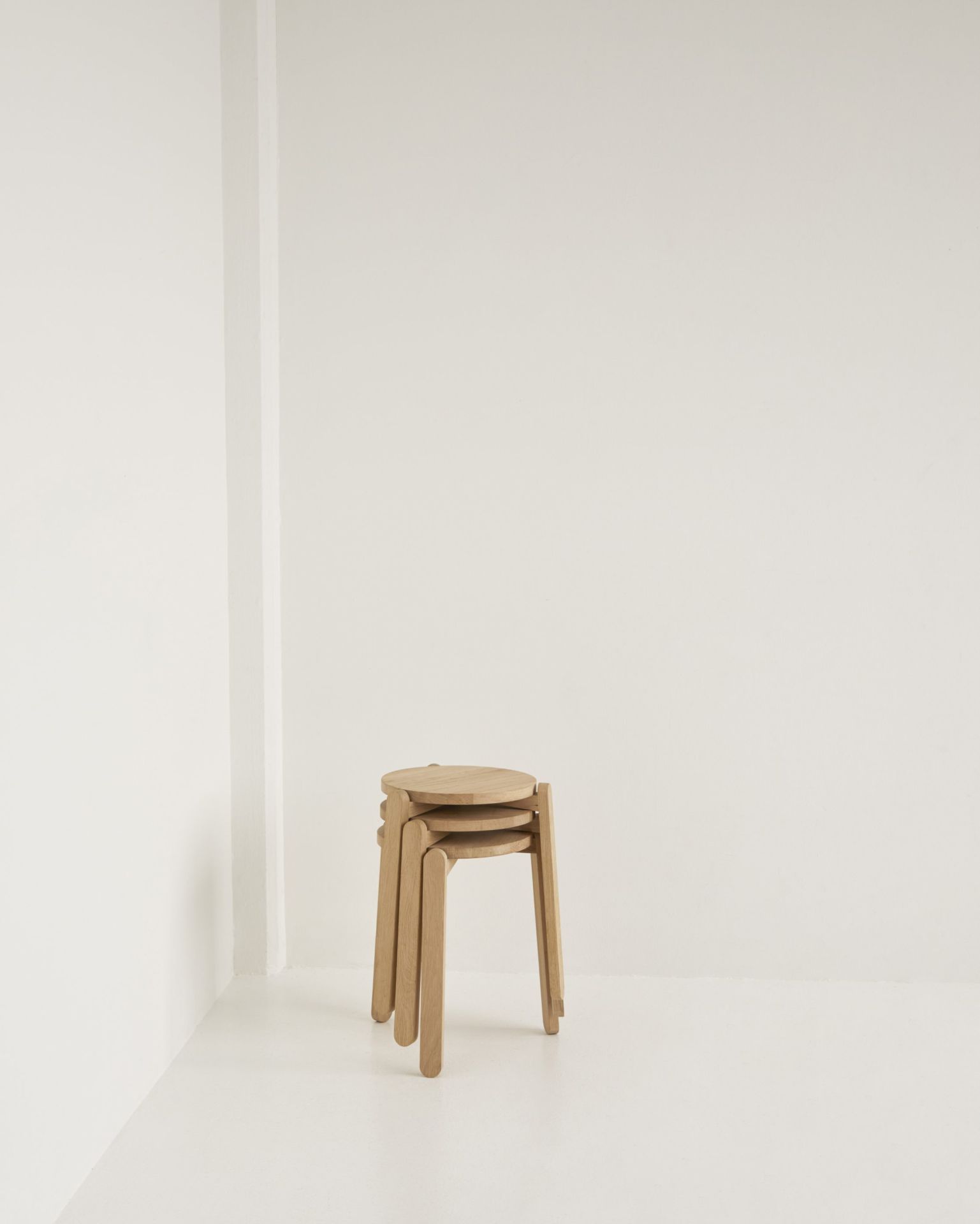 Drei Skagerak Nomad Stool Hocker aus hellem Holz gestapelt vor weißer Wand.