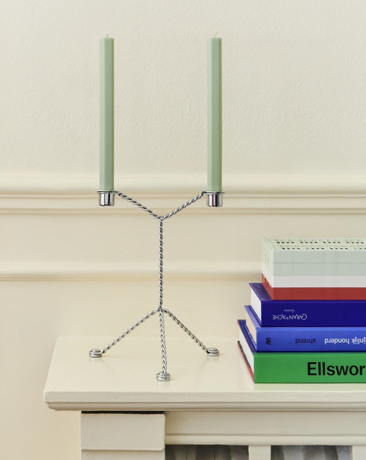 Hay Wire Candleholder Kerzenständer aus silbernem Draht mit zwei hellgrünen Kerzen auf einem Tisch.