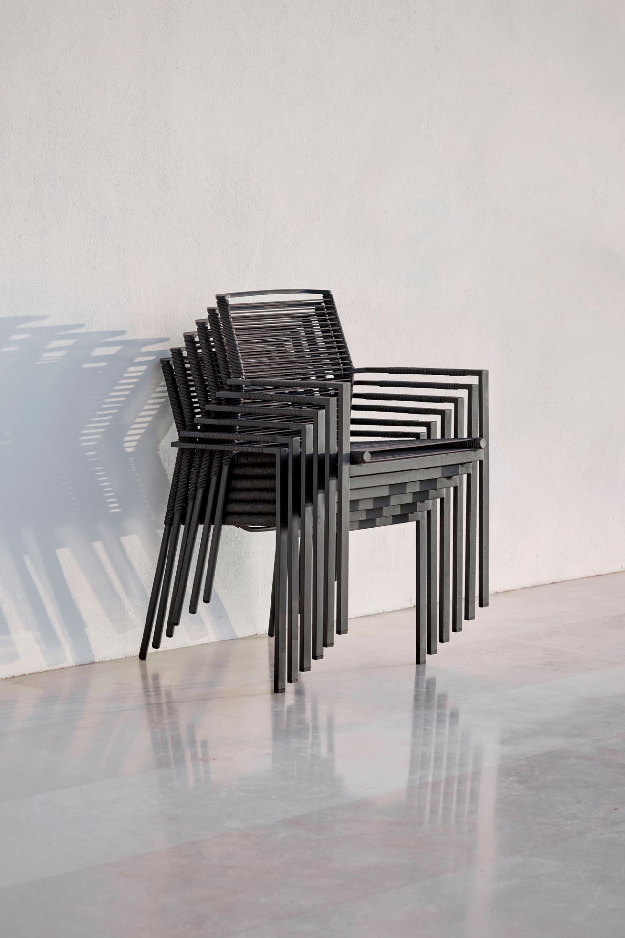 Stapel aus schwarzen Cane-Line Edge Outdoor Sesseln vor einer weißen Wand. Gartenmöbel.