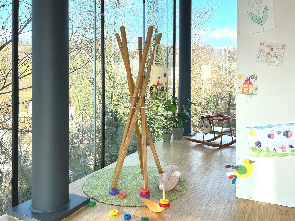 Mary for Kids Garderobenständer im Kinderzimmer: Holz-Garderobe mit Tasche, Spielzeug und kindlichen Zeichnungen im Hintergrund.