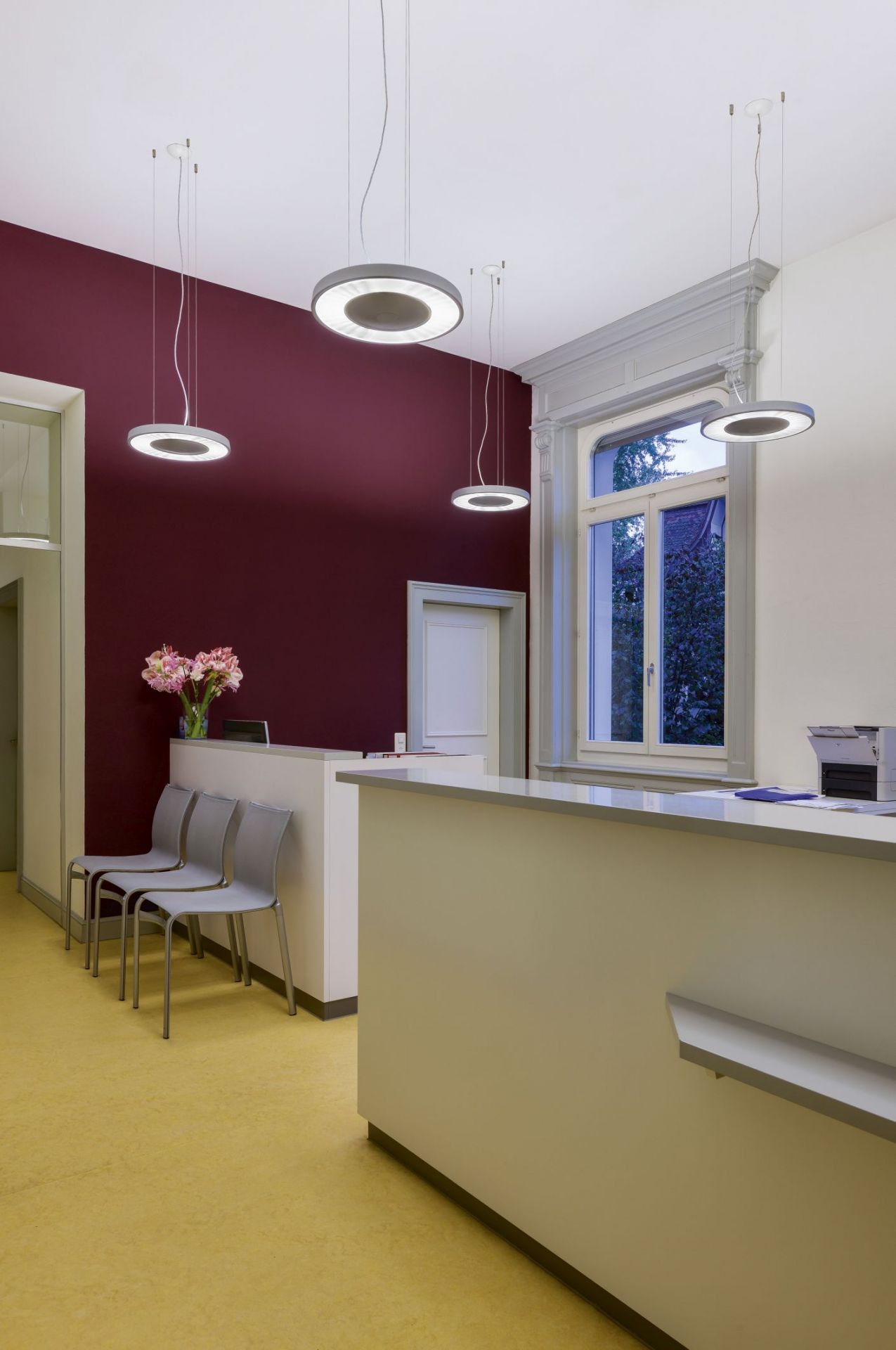 Helle Büroraum-Szene mit mehreren weißen Belux Disk Pendelleuchten 3000K über einem Empfangsbereich.